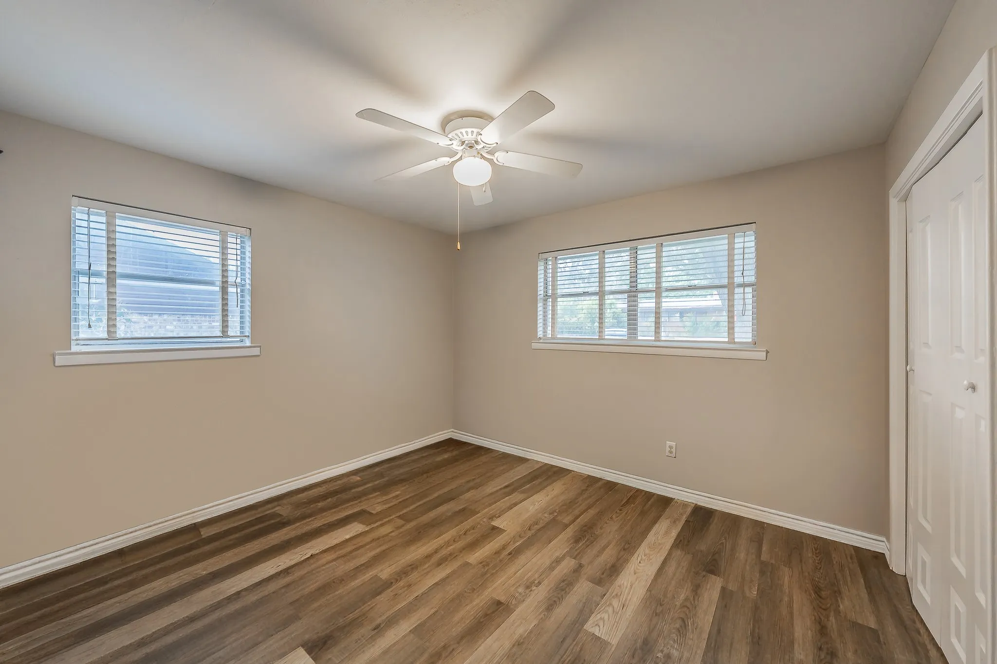 Wood-finish flooring, two windows with blinds, ceiling fan with integrated lighting, and a bi-fold closet door