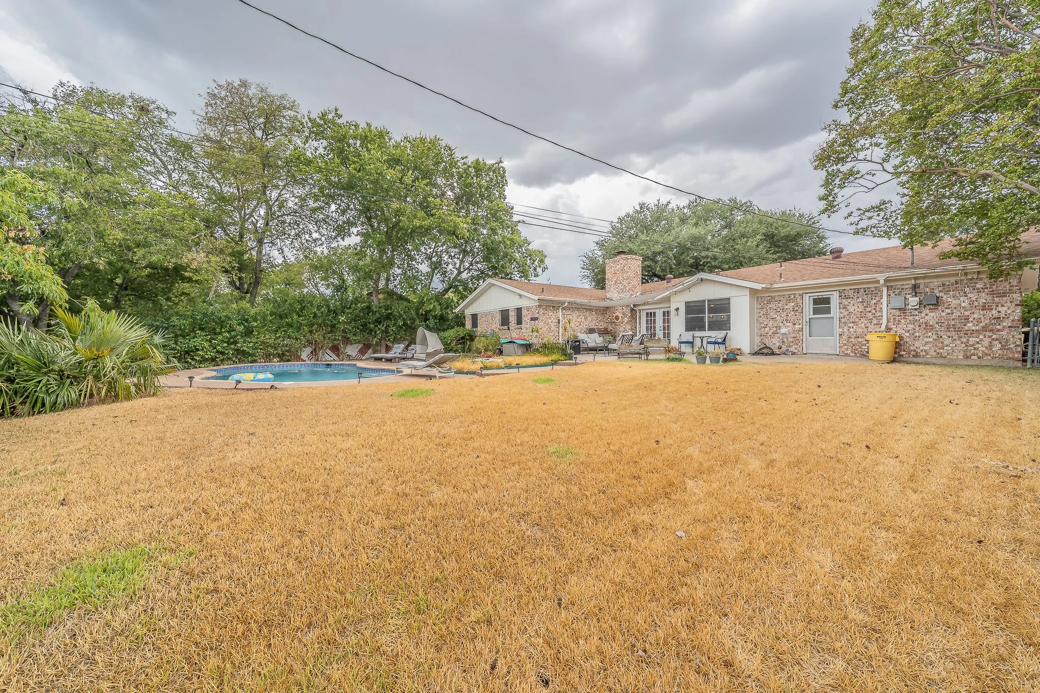 Expansive backyard featuring a built-in swimming pool with surrounding hardscaping, a stone exterior on the main residence, and a prominent brick chimney