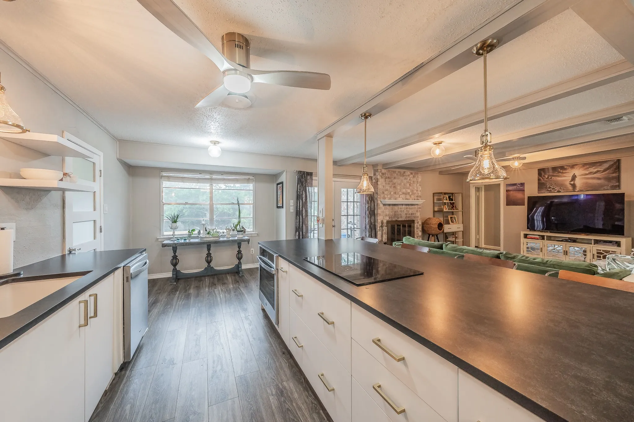 Expansive kitchen island with dark countertops, white cabinetry with brass-finish hardware, stainless steel built-in appliances, and wood-finish flooring