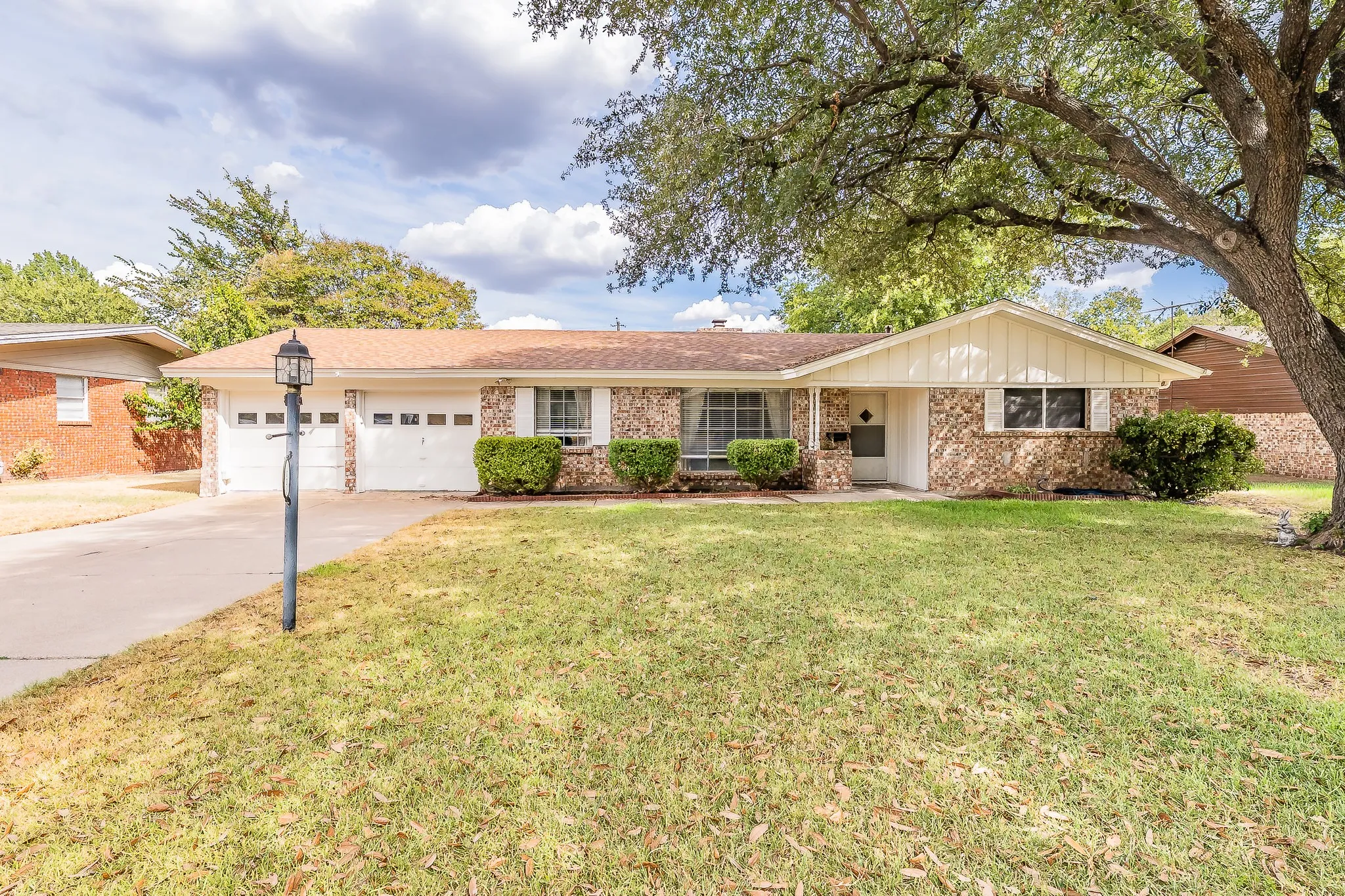 Brick exterior with a white storm door, double garage doors, and a mature tree