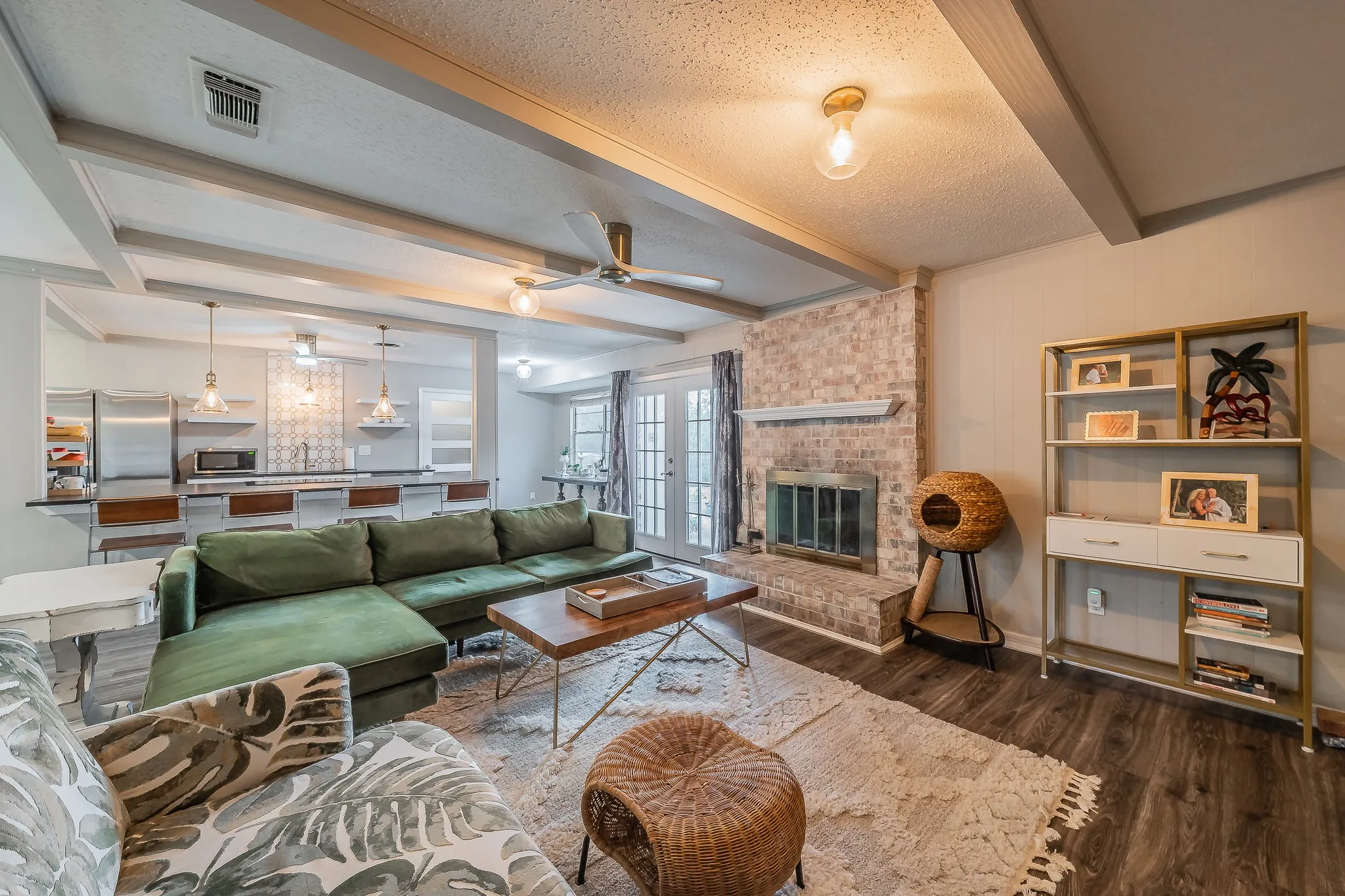 Wood-finish flooring, exposed ceiling beams, brick-faced fireplace with hearth, and French doors