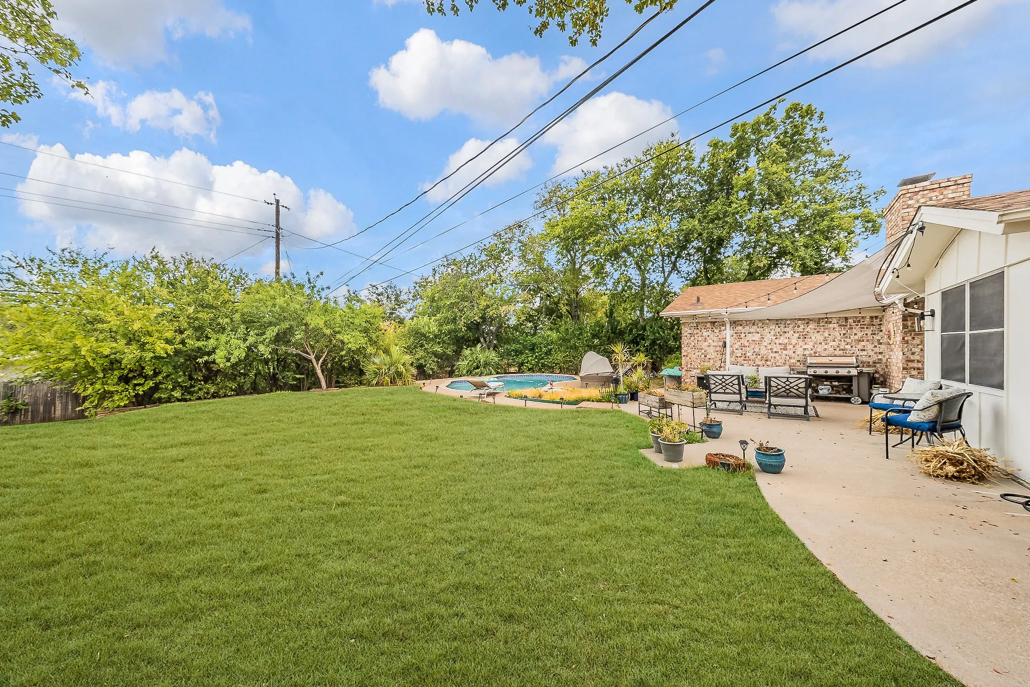 Expansive backyard featuring a large grass lawn, perimeter landscaping, and a concrete patio