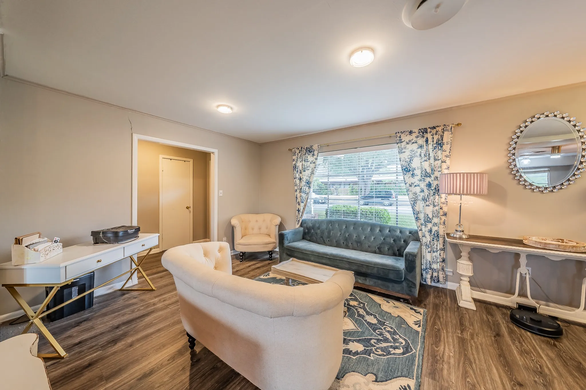 Sophisticated living space featuring a curved cream-upholstered sofa, wood-finish flooring throughout, and abundant natural light from large windows dressed in patterned curtains