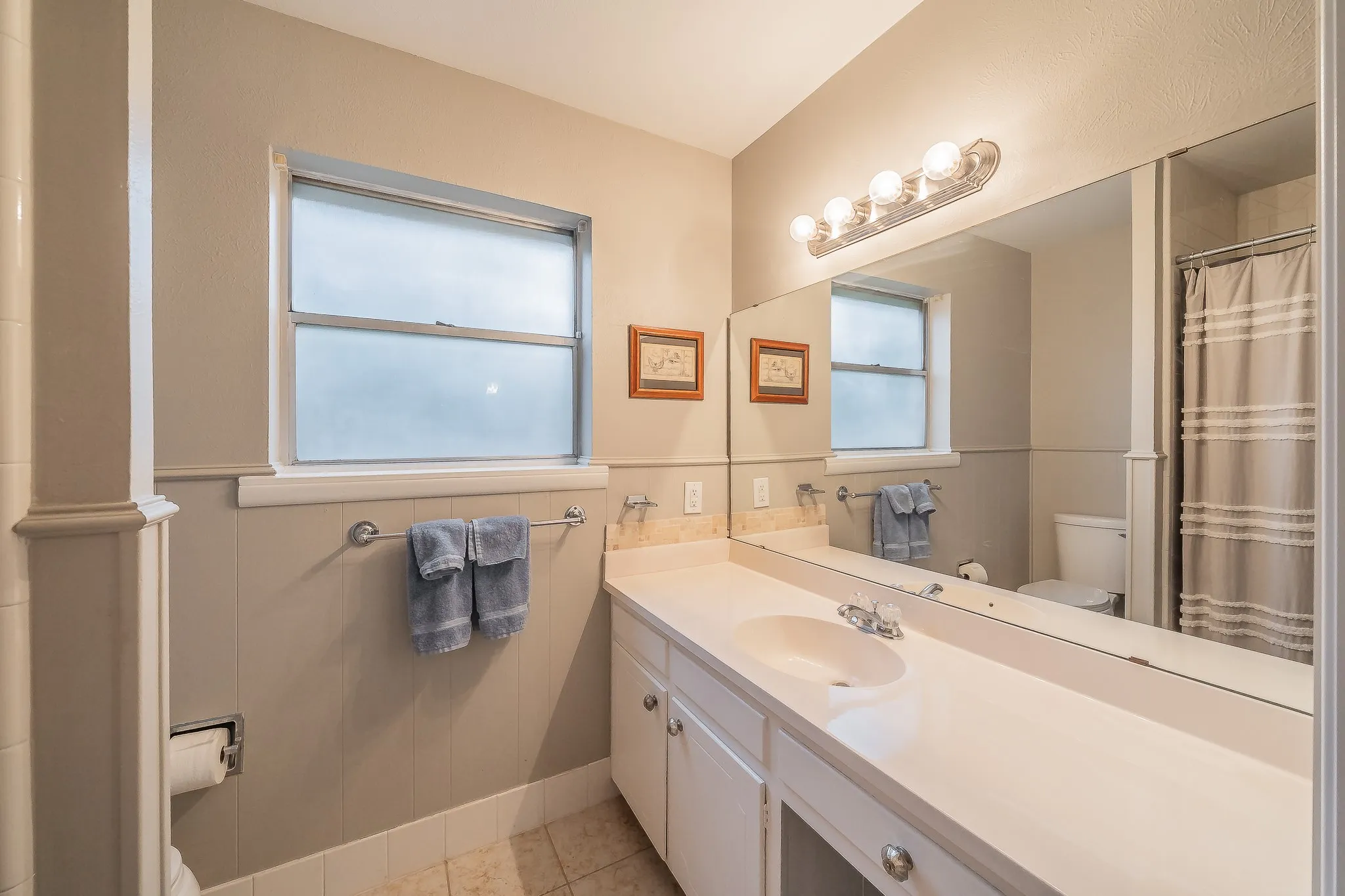 Vanity with integrated sink, expansive wall mirror, and overhead four-light fixture