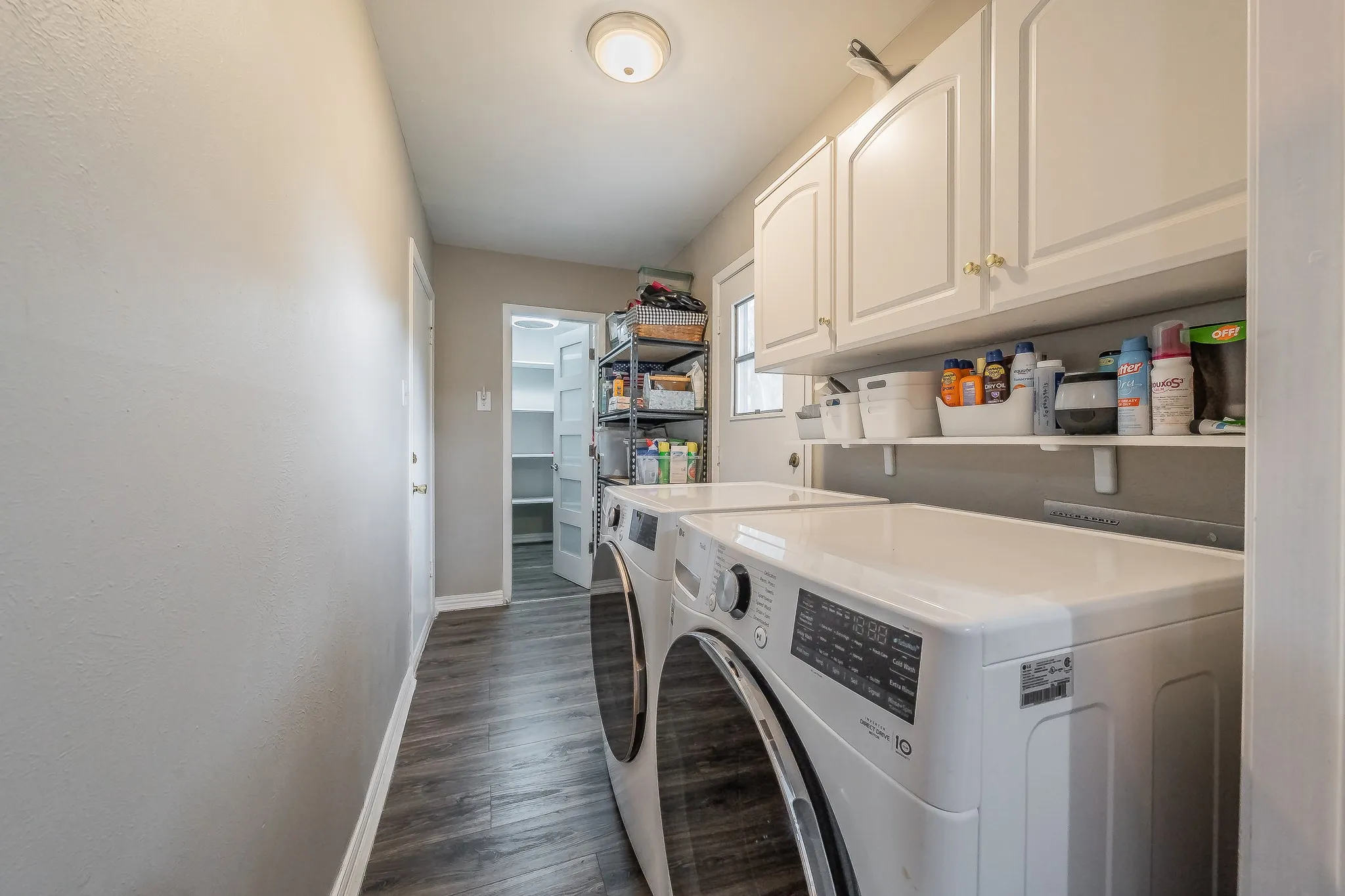 Laundry area featuring wood-finish flooring, overhead cabinetry, and wall-mounted shelving