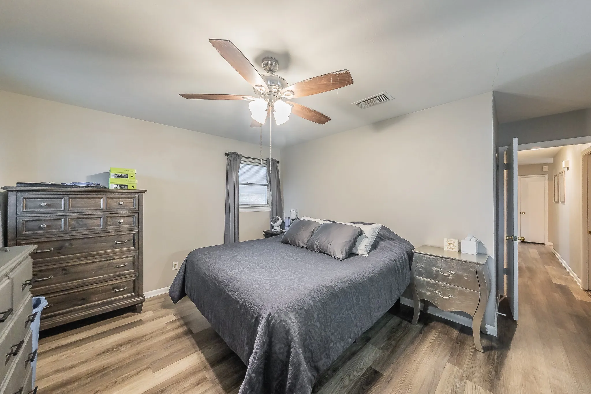 Wood-finish flooring throughout, complemented by a window with drapes, and a ceiling fan with integrated lighting