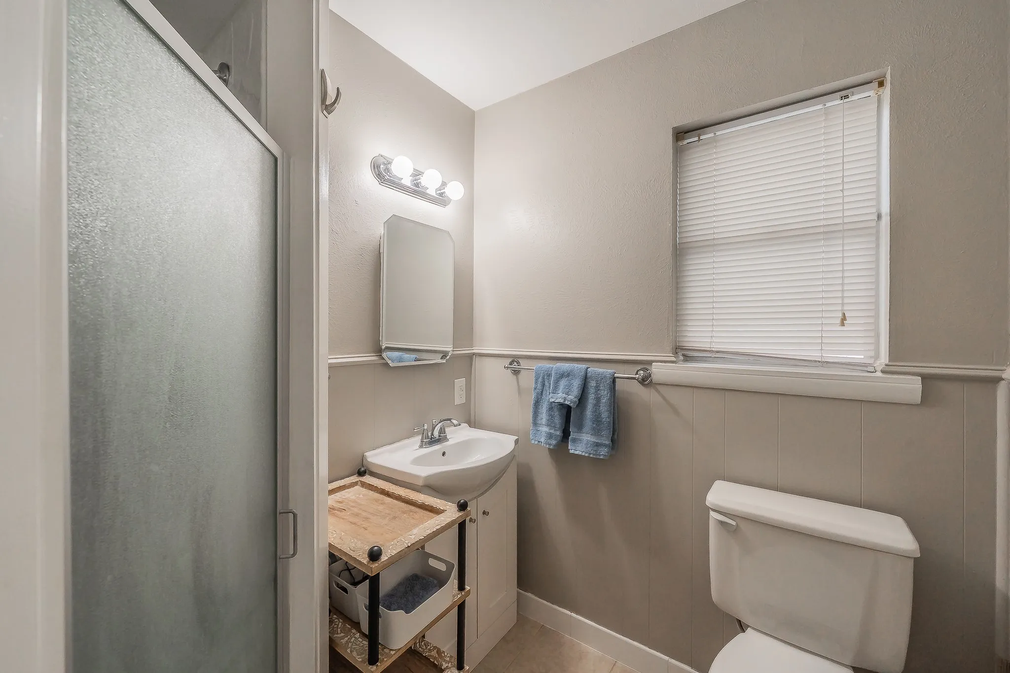 Frosted glass shower enclosure, single vanity with integrated sink, wall-mounted mirror, and natural light from the window