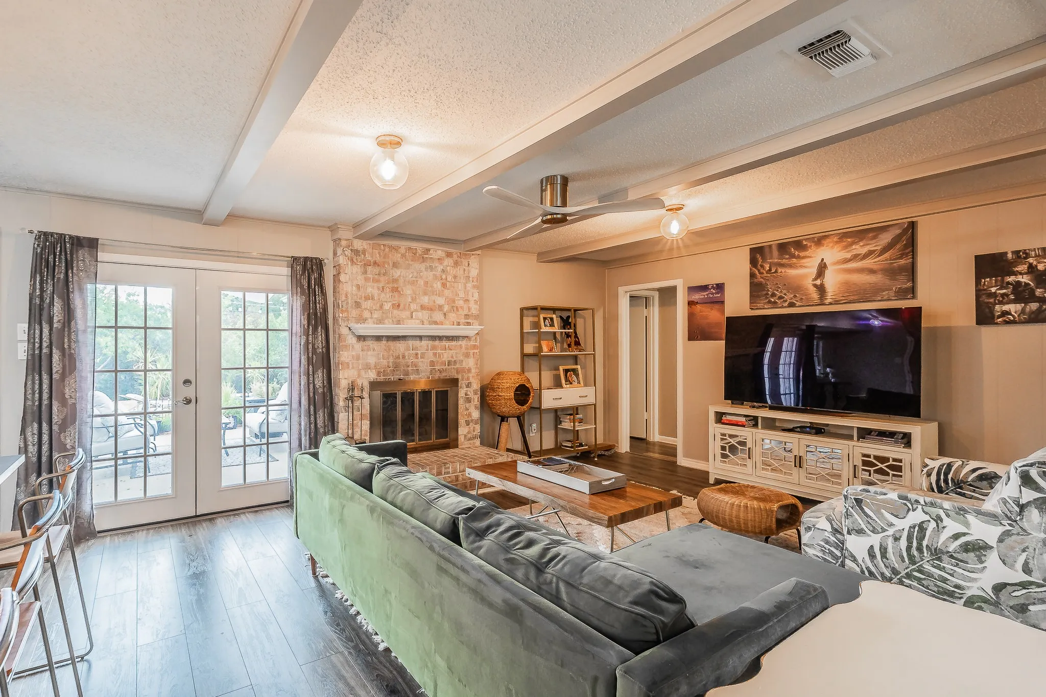 Spacious living room featuring hardwood flooring, a brick fireplace with built-in shelving, a wall-mounted flat-screen television with cabinetry, and French doors opening to the exterior