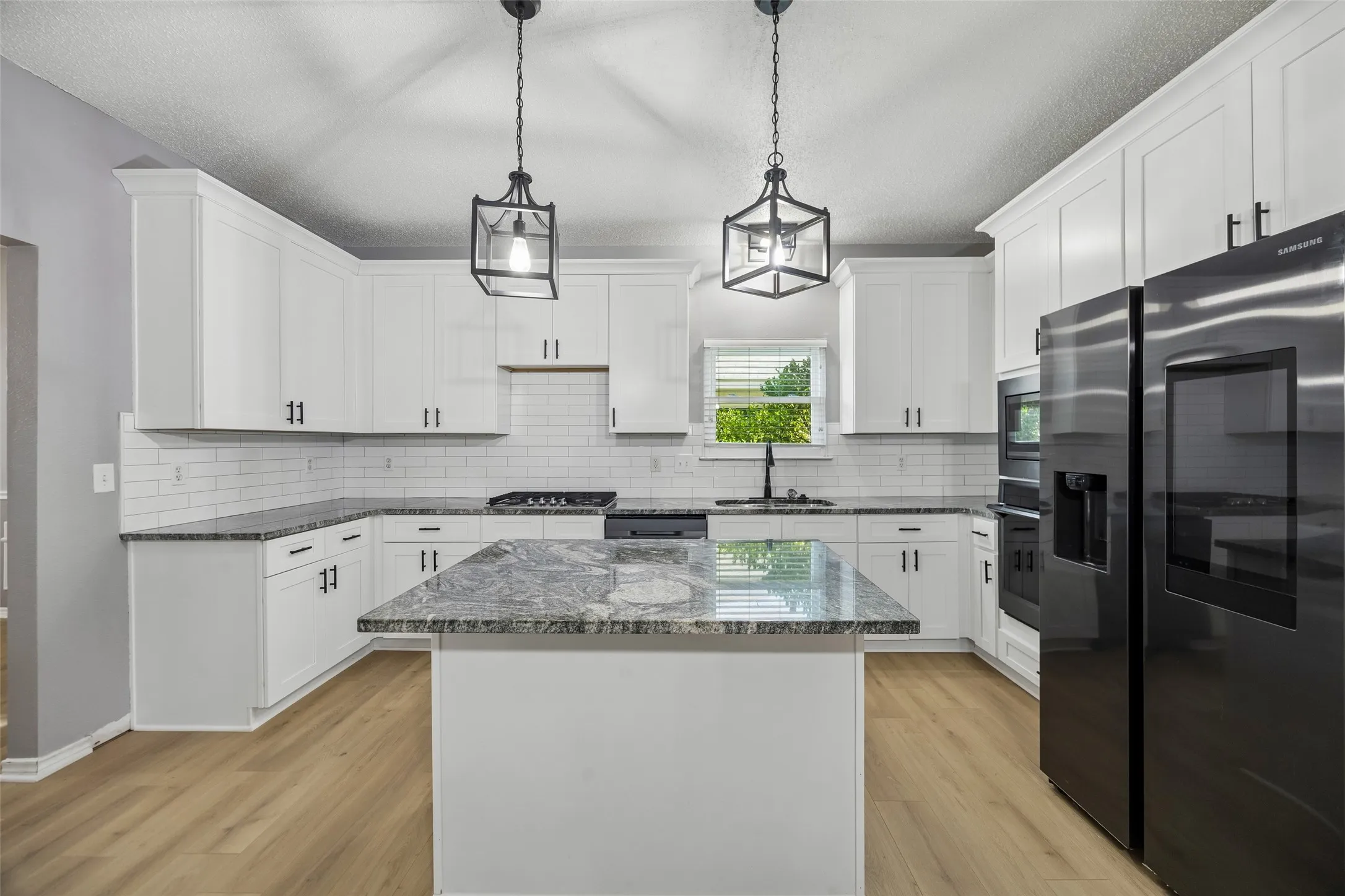 Kitchen featuring white shaker cabinetry, dark stone countertops, stainless steel appliances, and wood-finish flooring