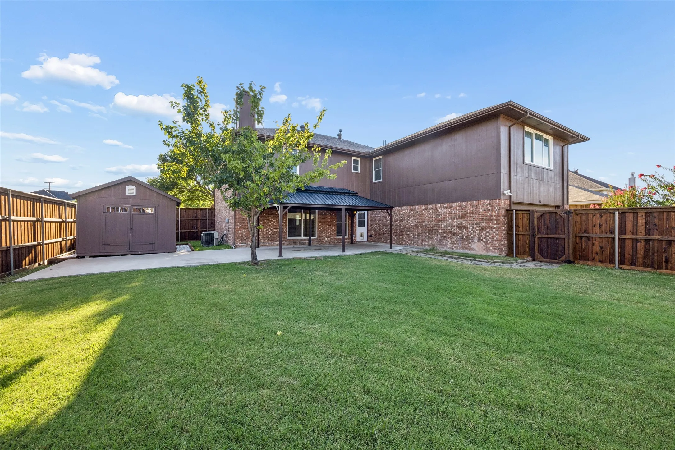 Spacious backyard featuring a covered patio, expansive lawn, and a detached storage shed