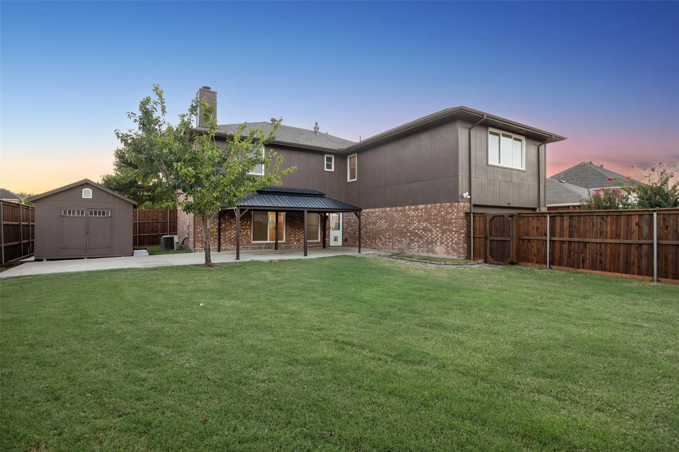 Expansive green lawn with a covered patio, wood privacy fencing, and a detached storage shed