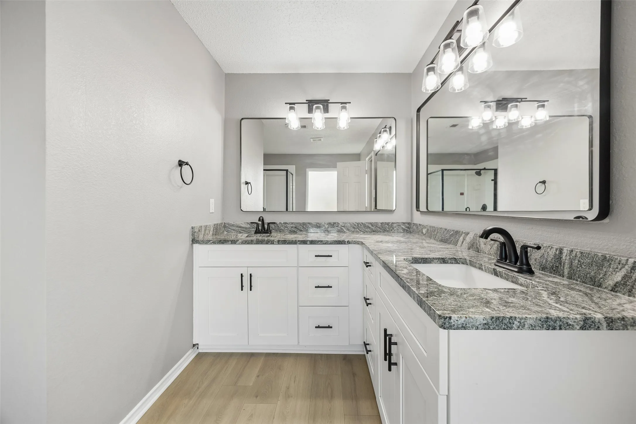 Dual vanity with granite countertops, white cabinetry, undermount sinks, matte black hardware, and wood-finish flooring