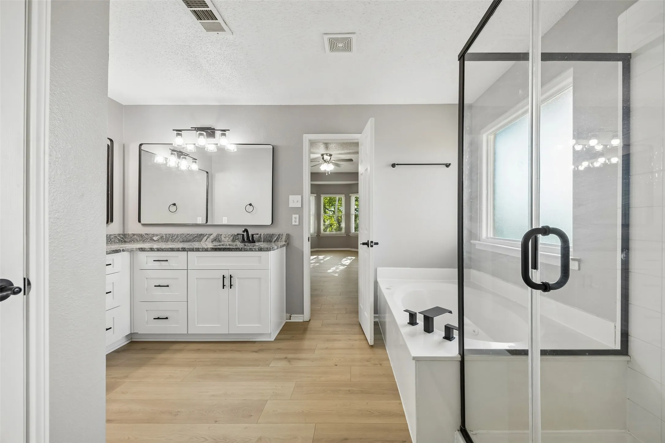 Dual vanity with granite-style countertop, white cabinetry, wood-finish flooring, and a glass-enclosed shower