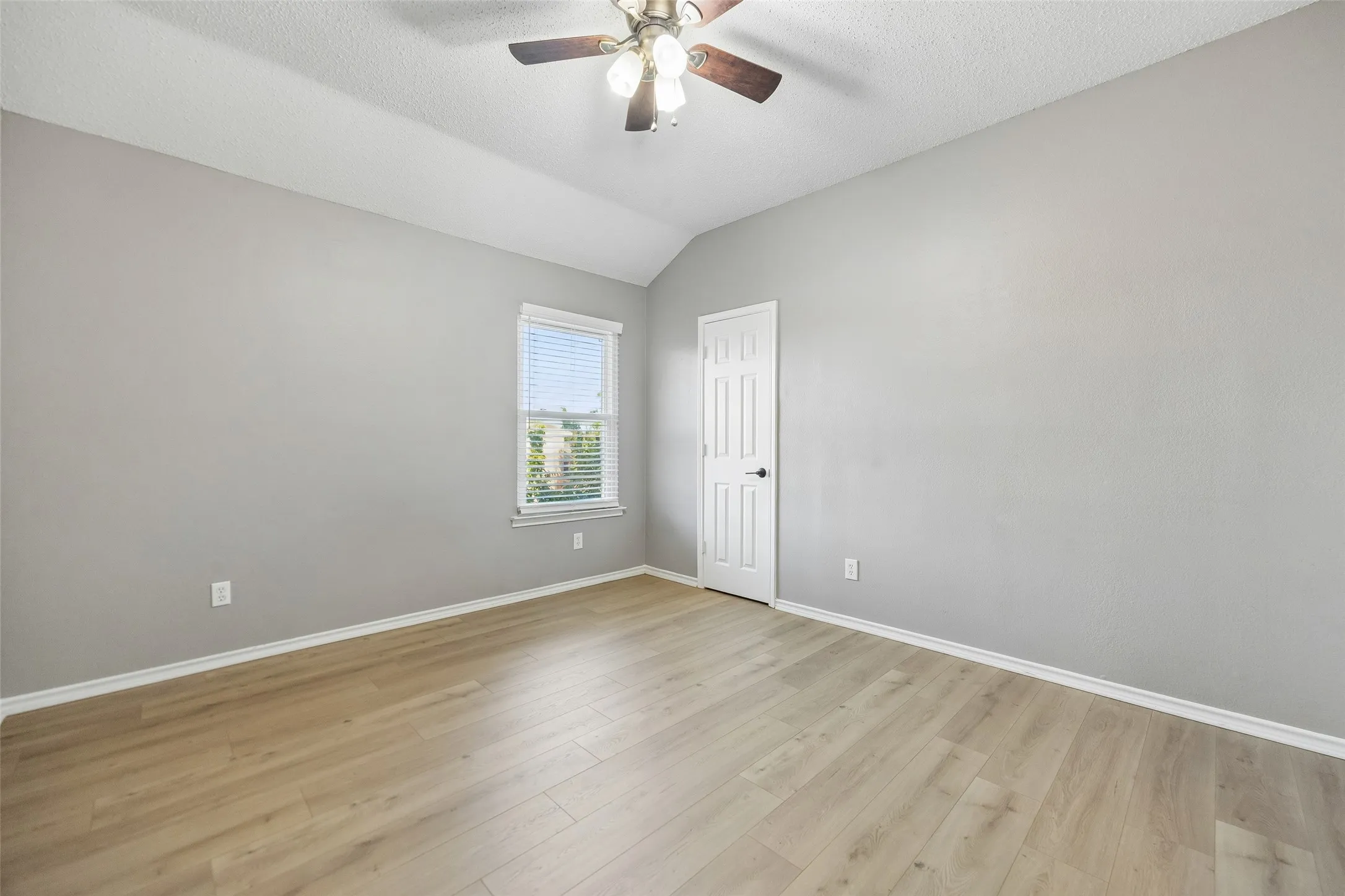 Vaulted ceiling with a ceiling fan, wood-finish flooring, and a paneled door