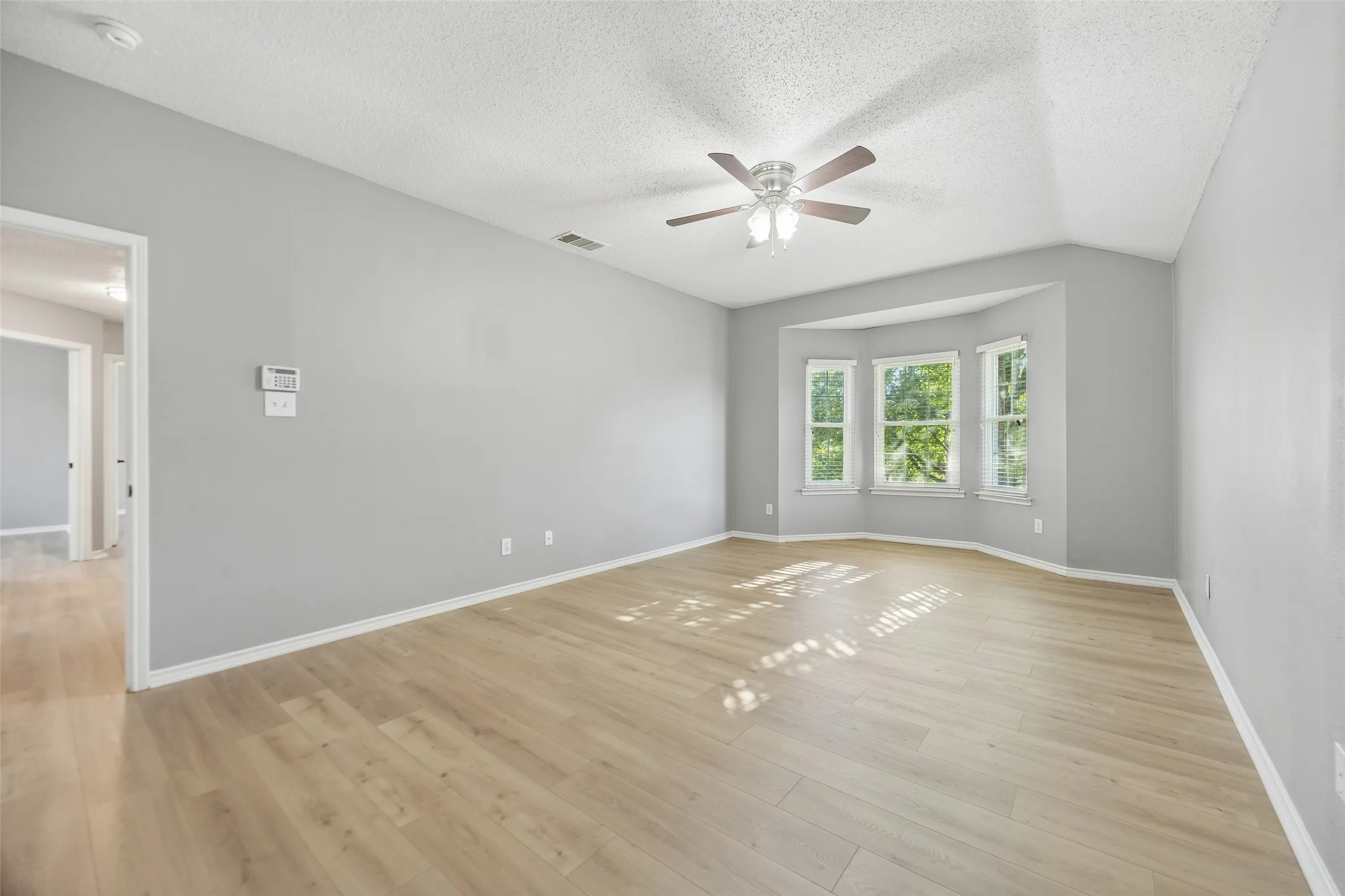 Expansive room featuring wood-finish flooring, a ceiling fan with integrated lighting, and a bay window ensemble