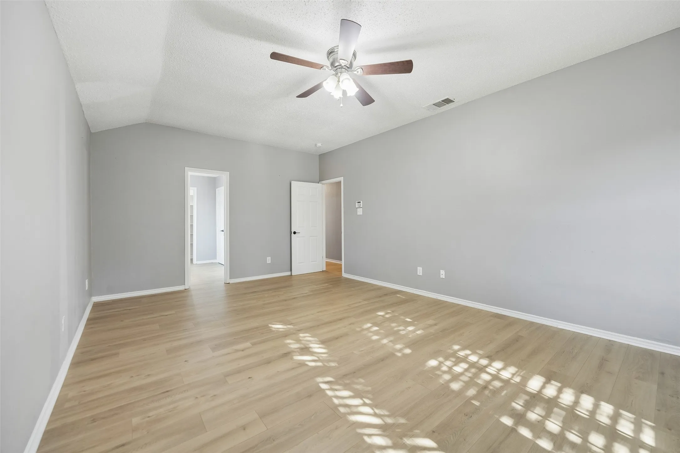Spacious room featuring vaulted ceilings, wood-finish flooring, and a ceiling fan