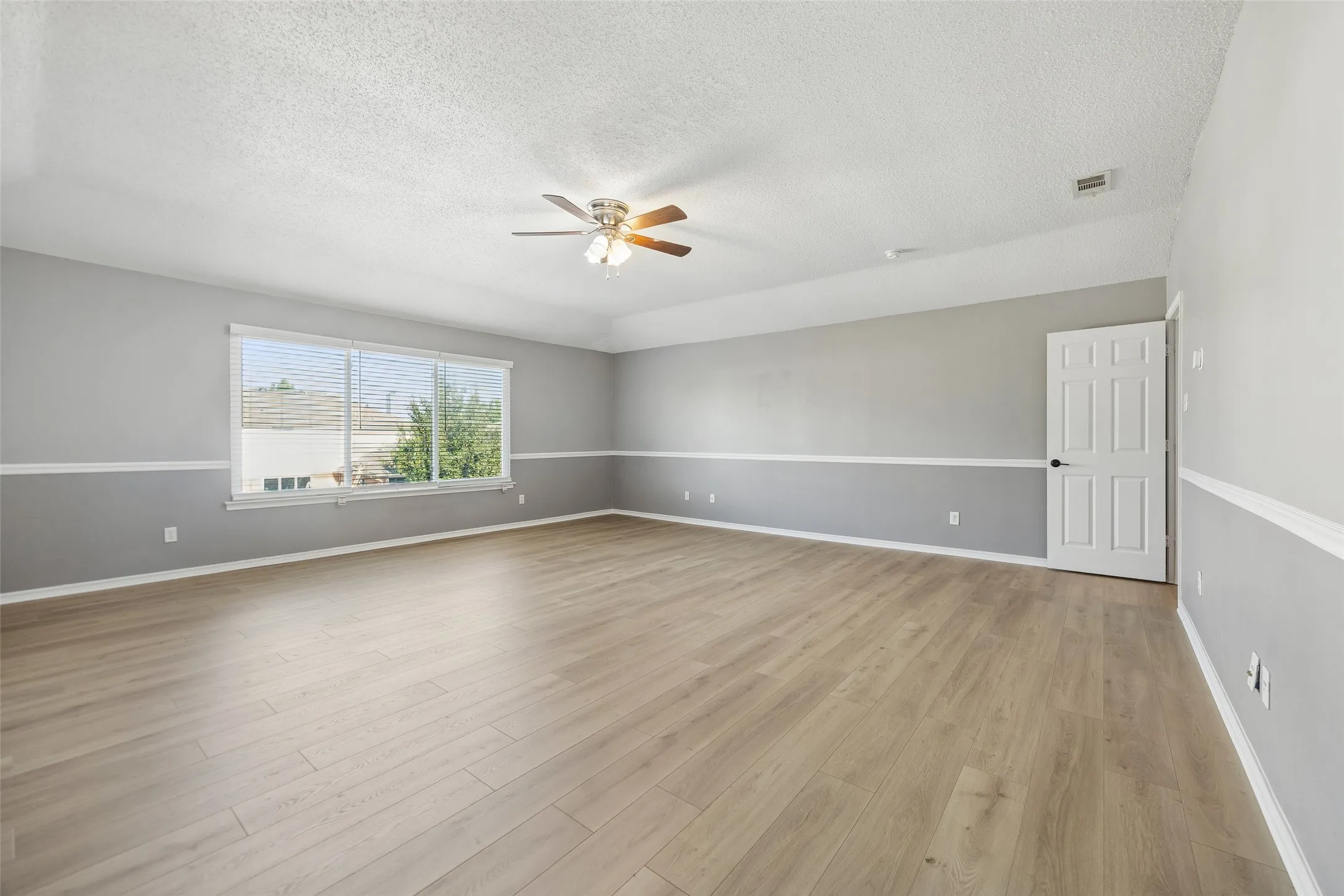 Expansive room featuring wood-finish flooring, a ceiling fan, and a large window with horizontal blinds