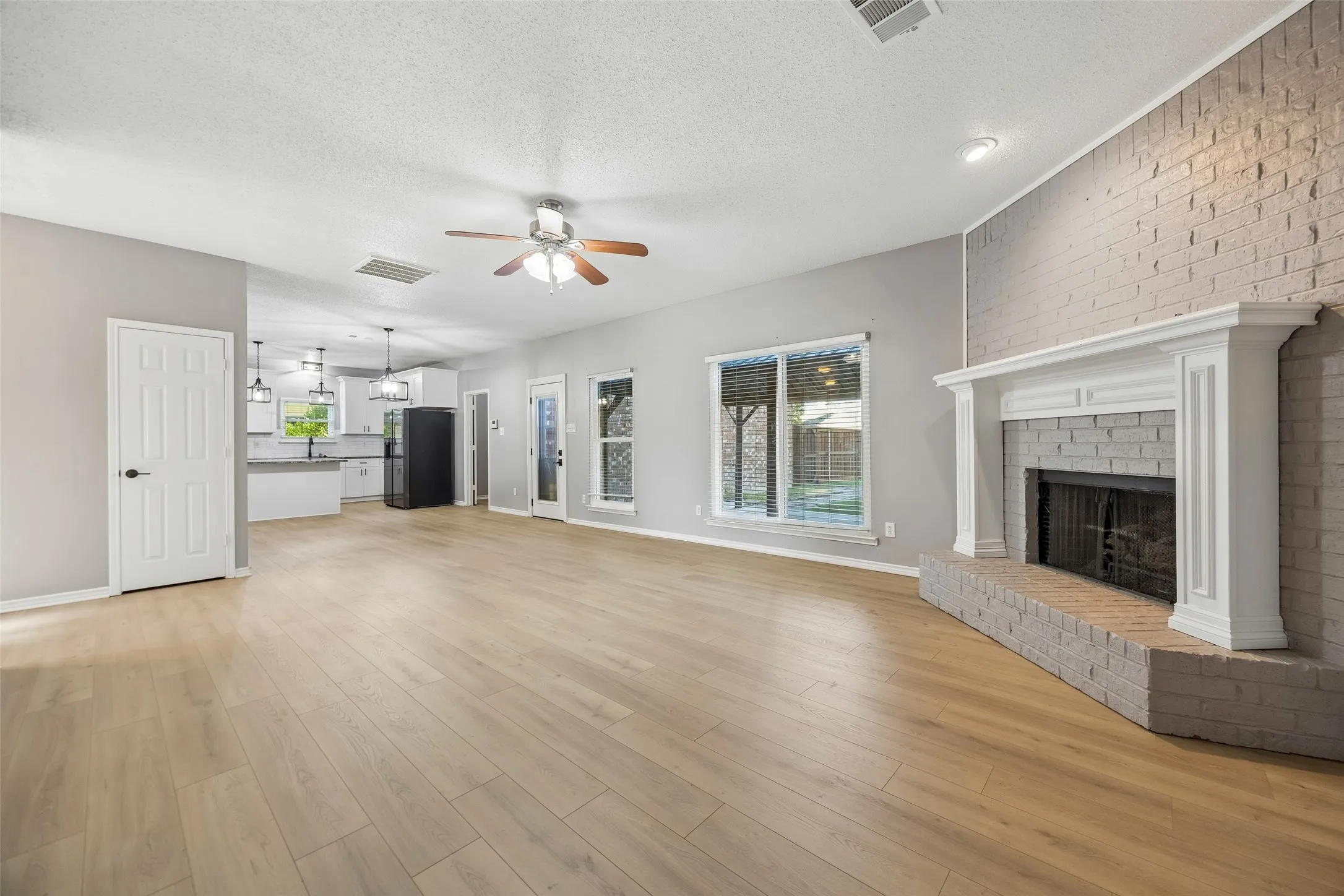 Spacious living area featuring wood-finish flooring, a painted brick fireplace with a white mantel, and a ceiling fan