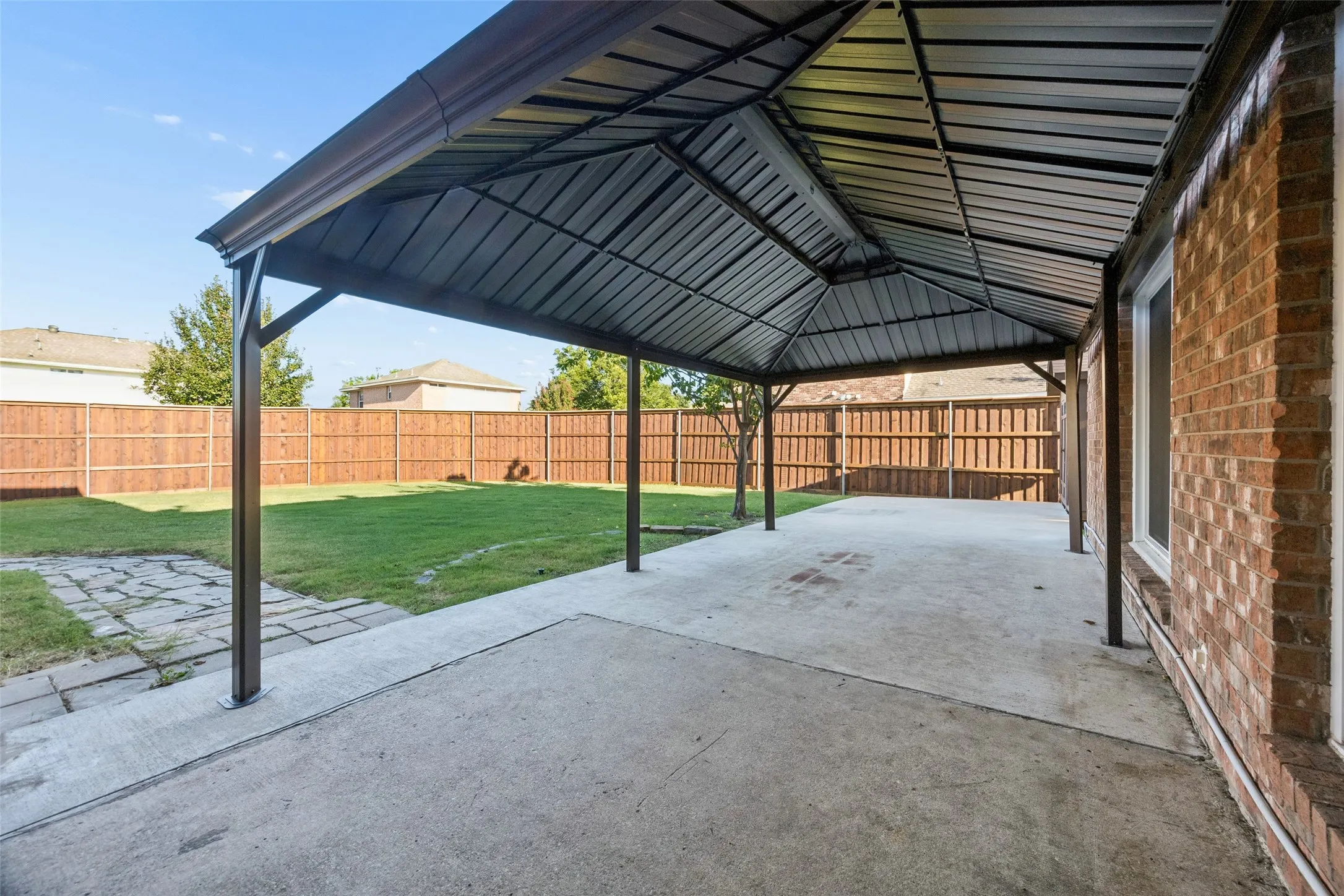 Expansive covered patio with steel beam construction and corrugated metal roof, offering generous shelter over a concrete foundation