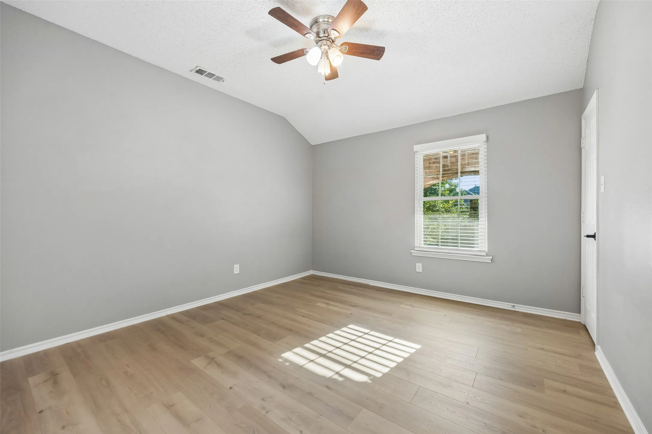 Vaulted ceiling with a ceiling fan, light wood-finish flooring, and a window with blinds
