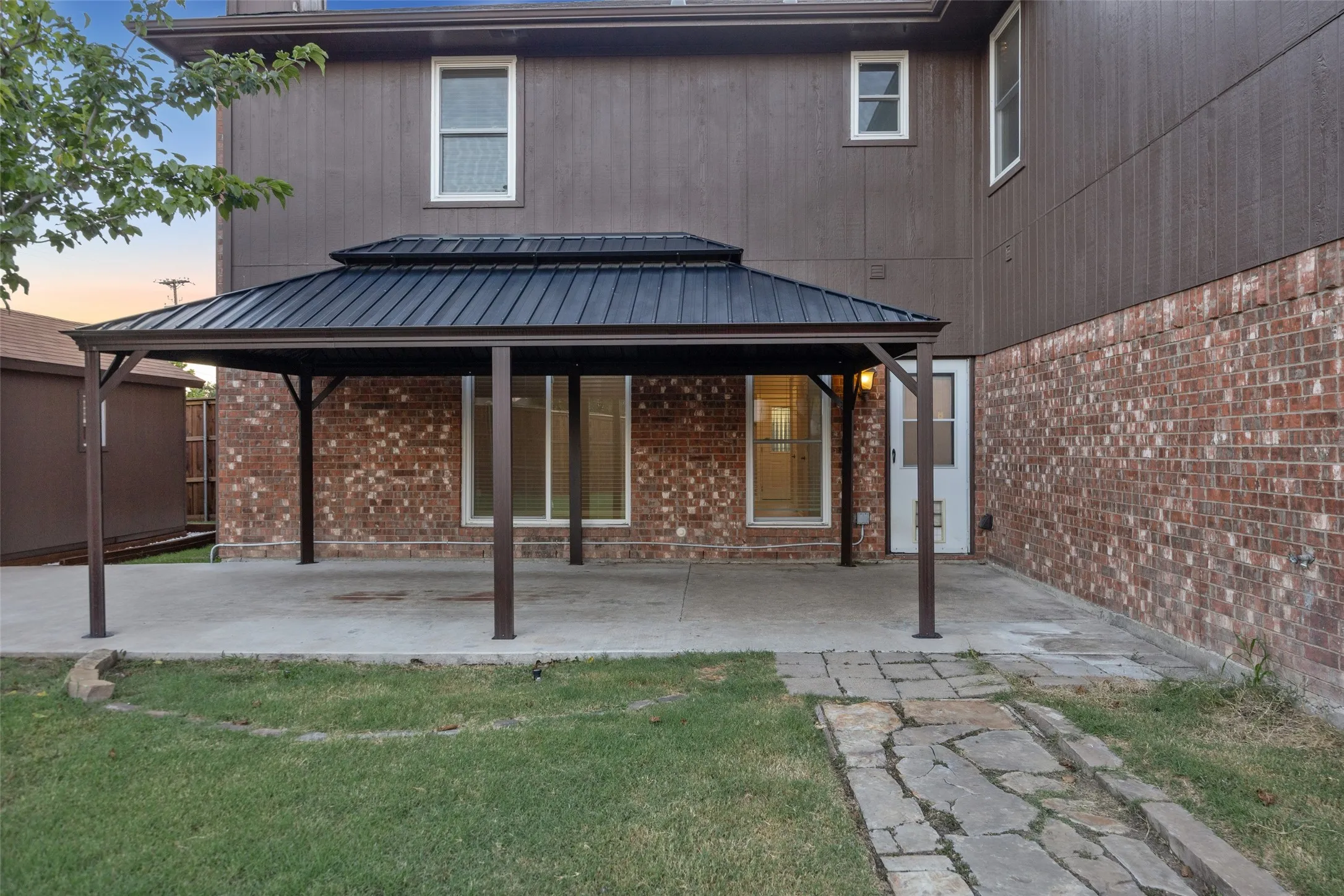 Spacious concrete patio with a tiered metal gazebo, brick exterior, and a stone walkway
