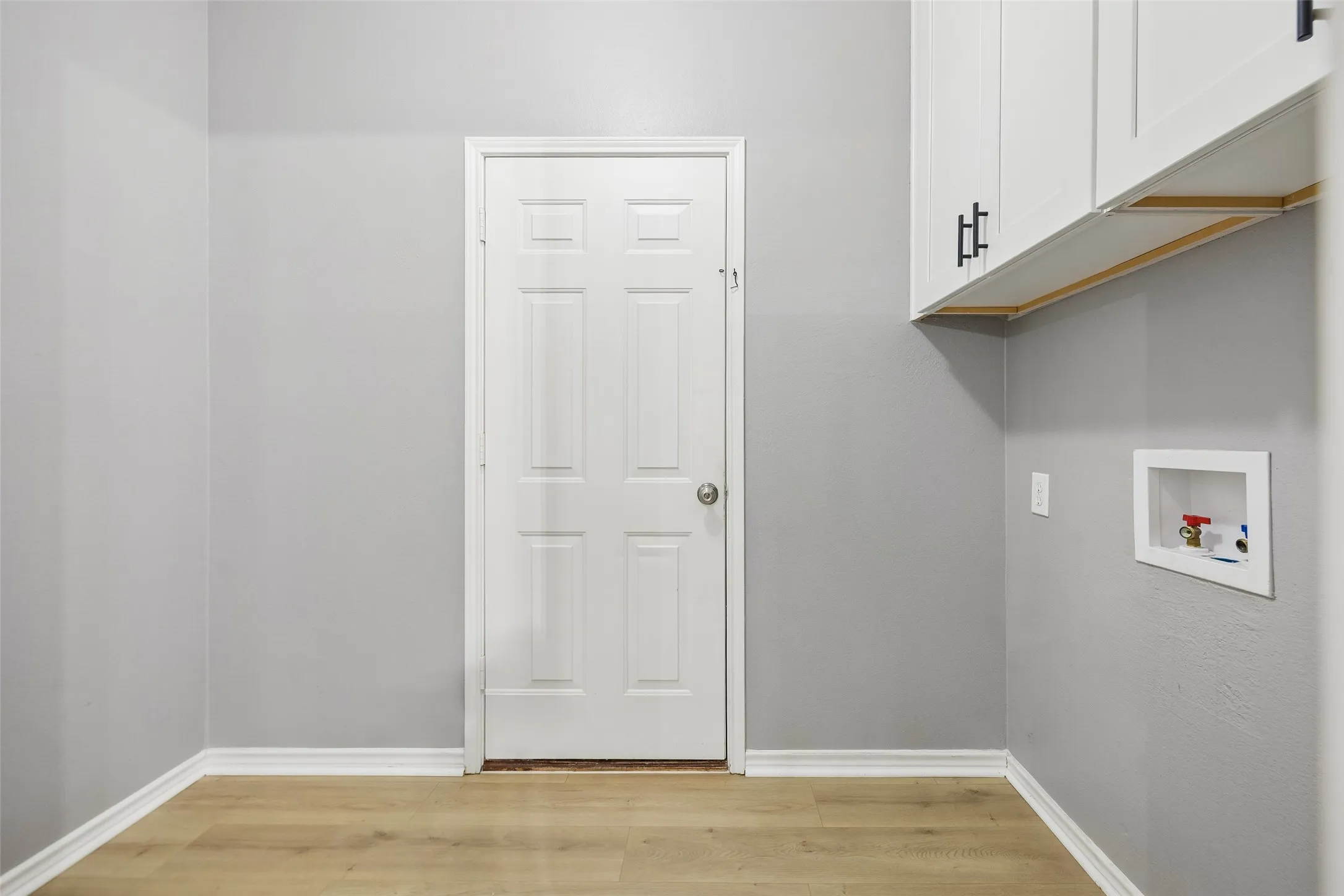 White paneled door with a silver knob, wood-finish flooring, and crisp white trim