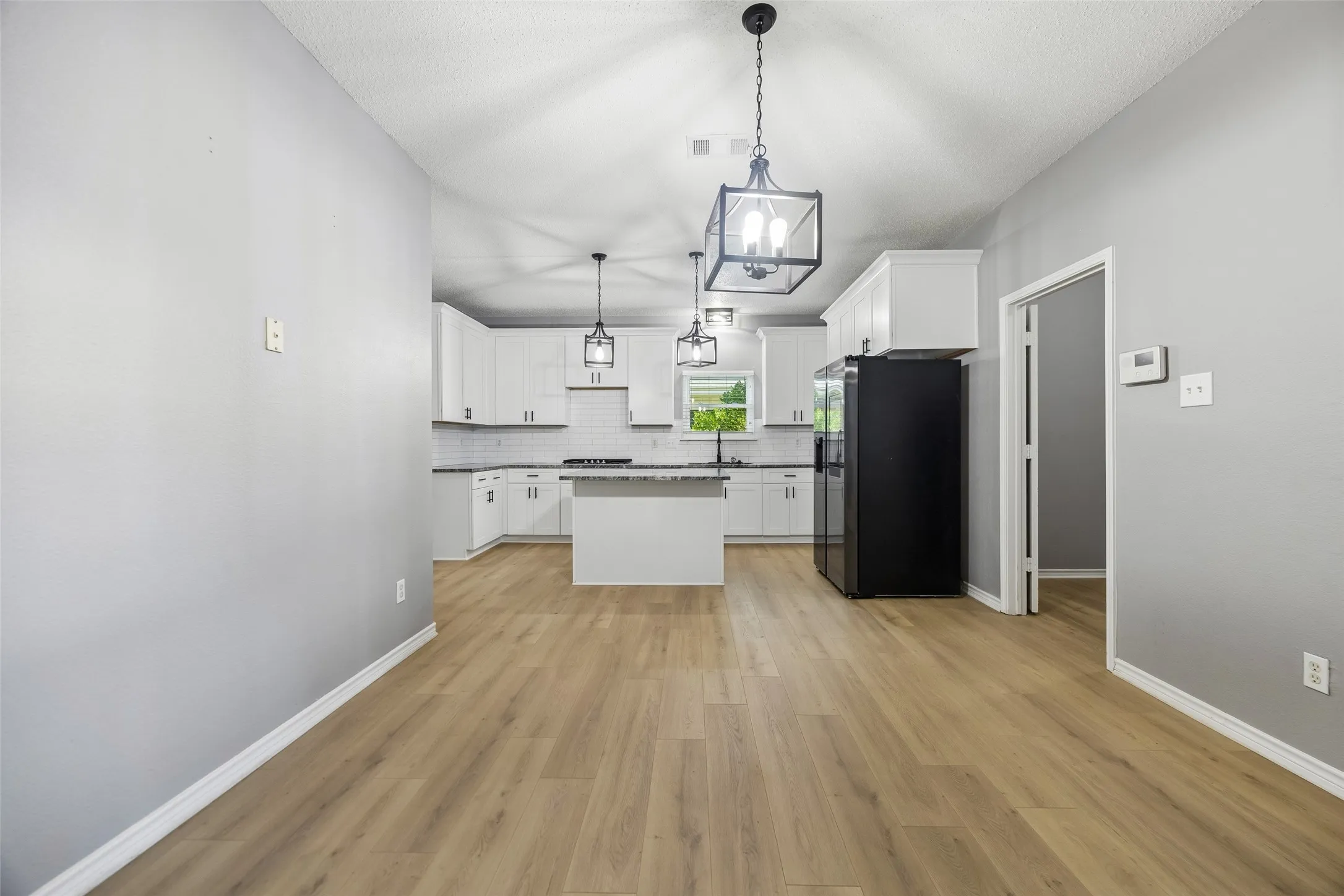 Wood-finish flooring, white cabinetry, island with countertop, black appliances, and pendant lighting