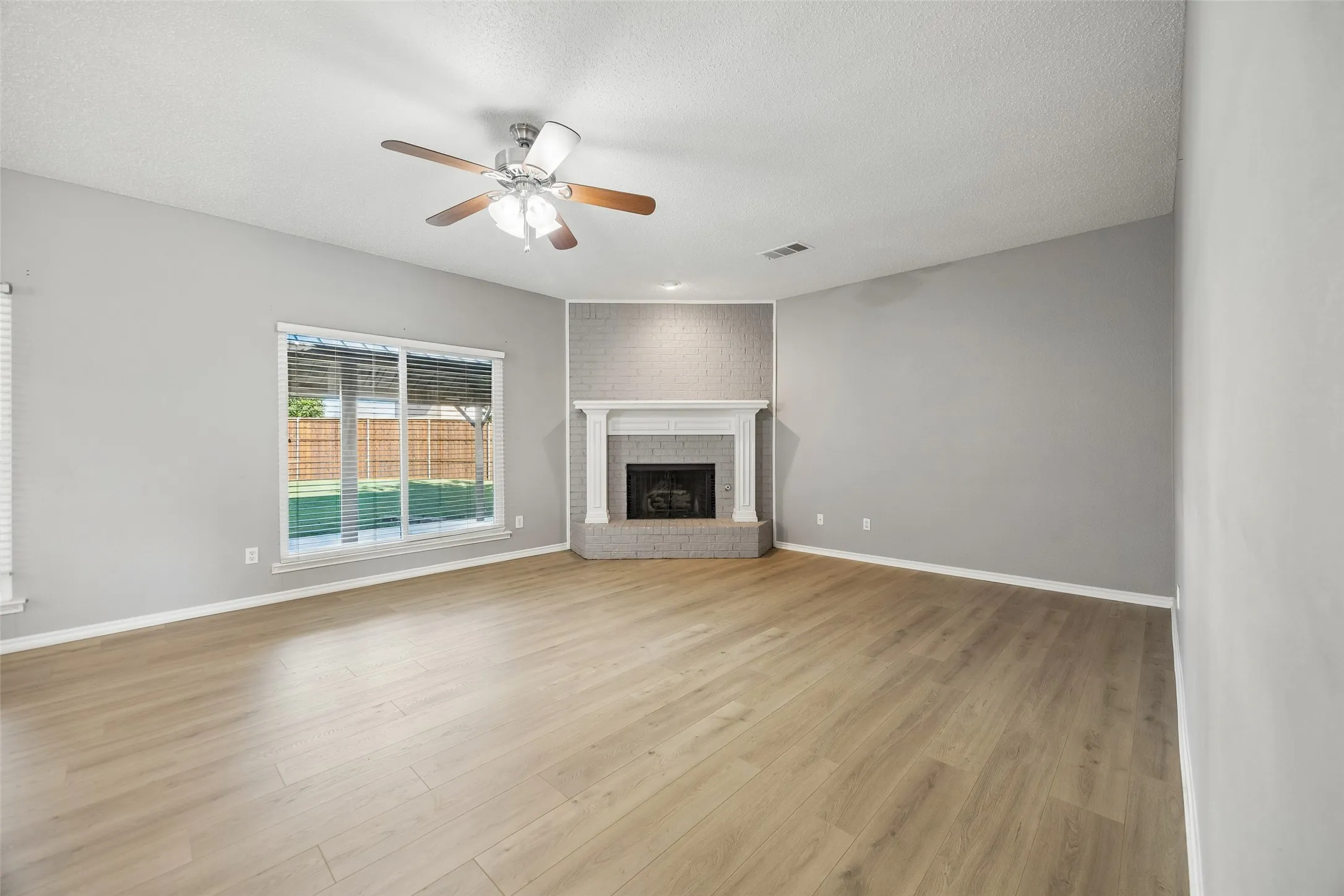 Wood-finish flooring, corner fireplace with a white mantel, ceiling fan with light fixture, and a sliding glass door