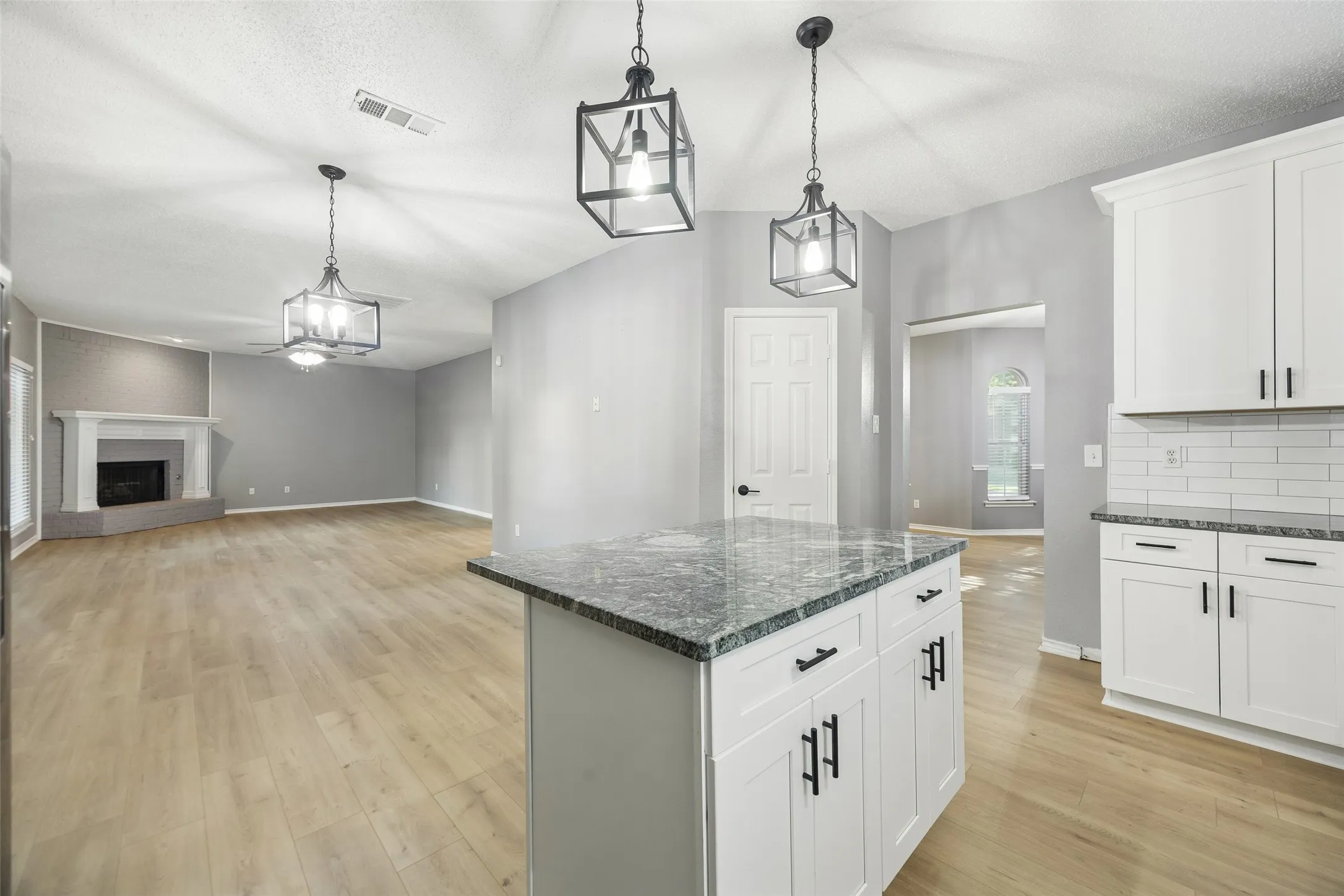 Kitchen island with stone countertop and white cabinetry, wood-finish flooring, white subway tile backsplash, and a corner fireplace with a white mantel