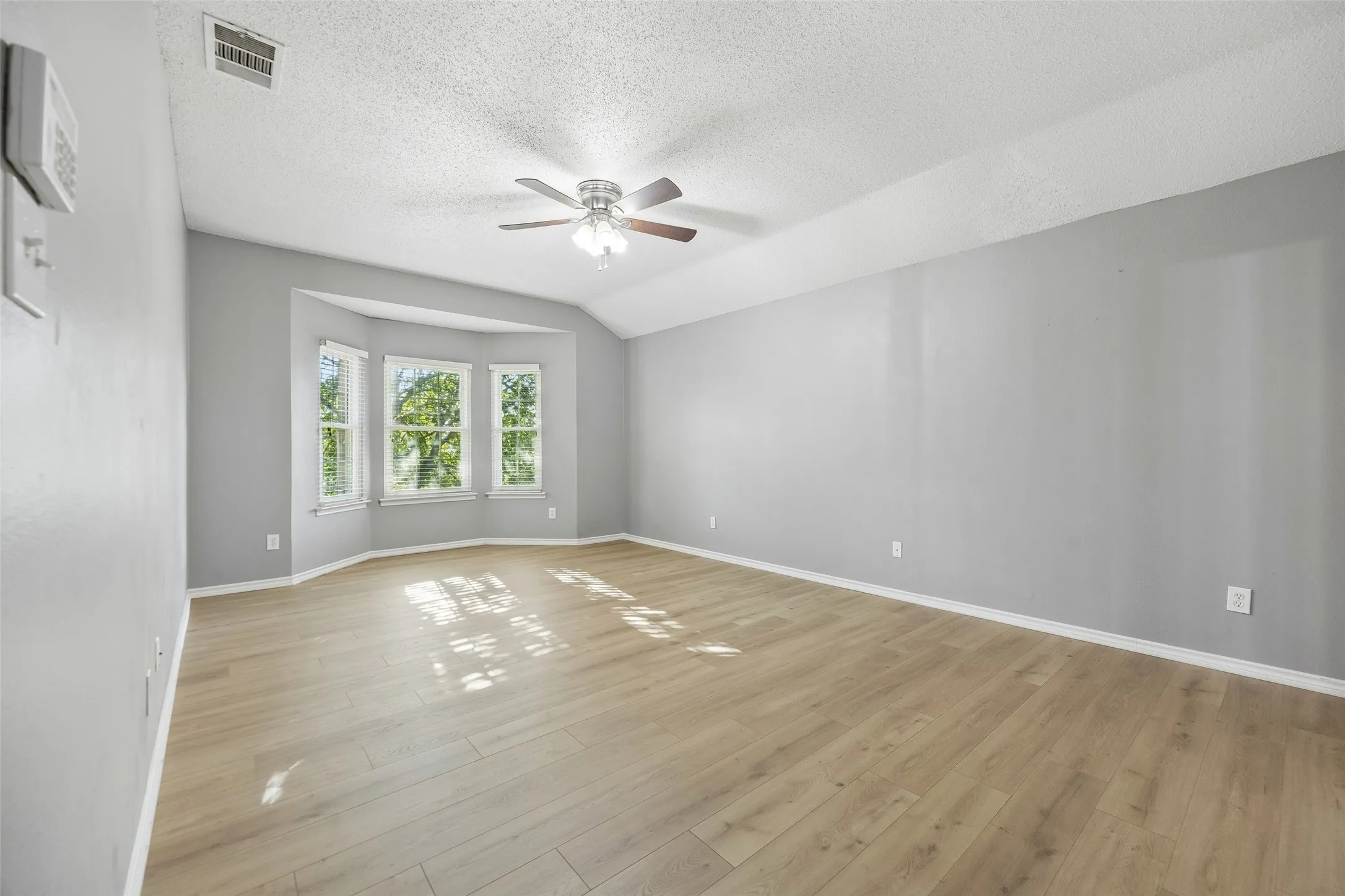 Vaulted ceiling, ceiling fan, wood-finish flooring, bay window, and light gray wall paint
