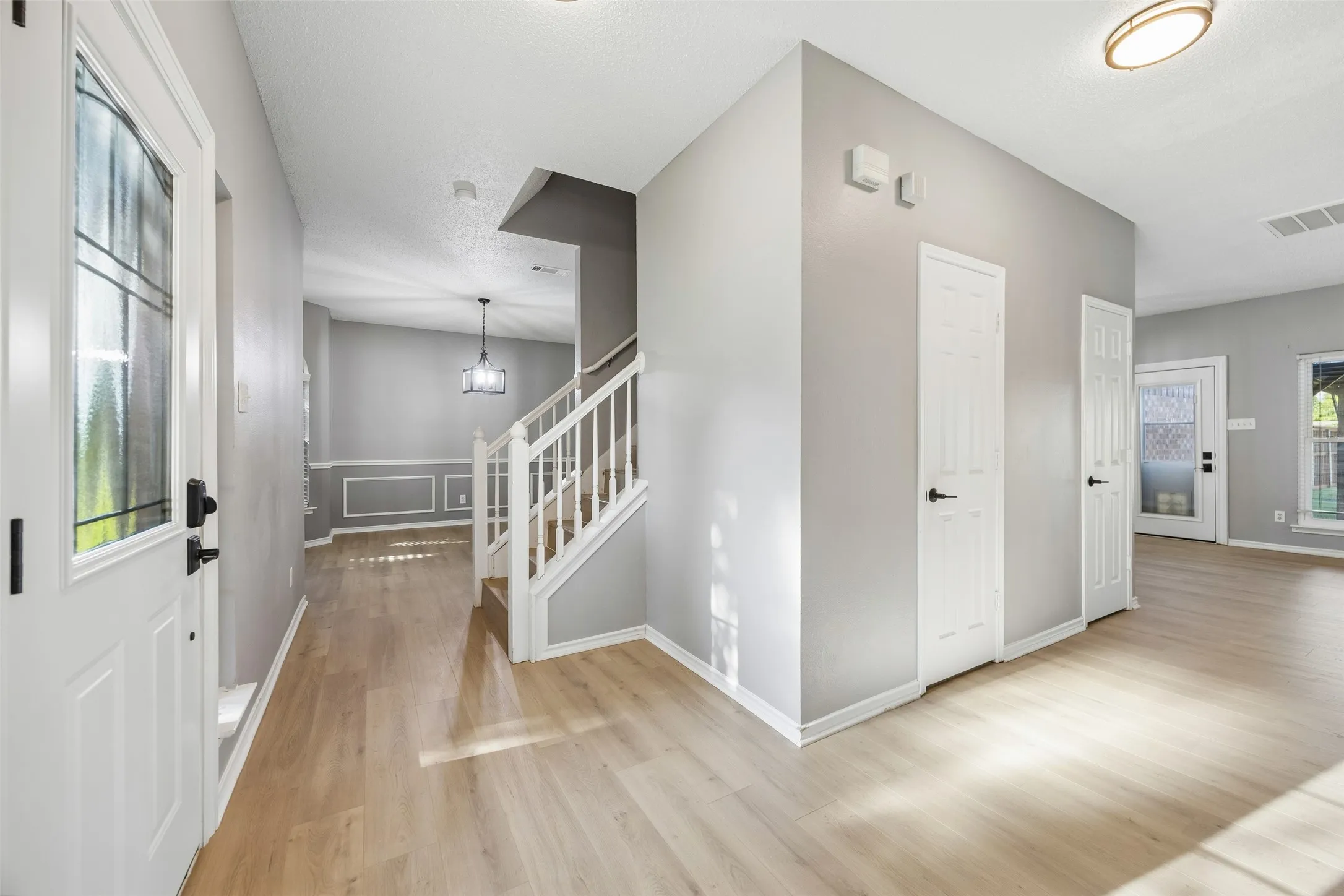 Entryway with wood-finish flooring, white paneled doors, staircase with white railing, and flush-mount ceiling lighting