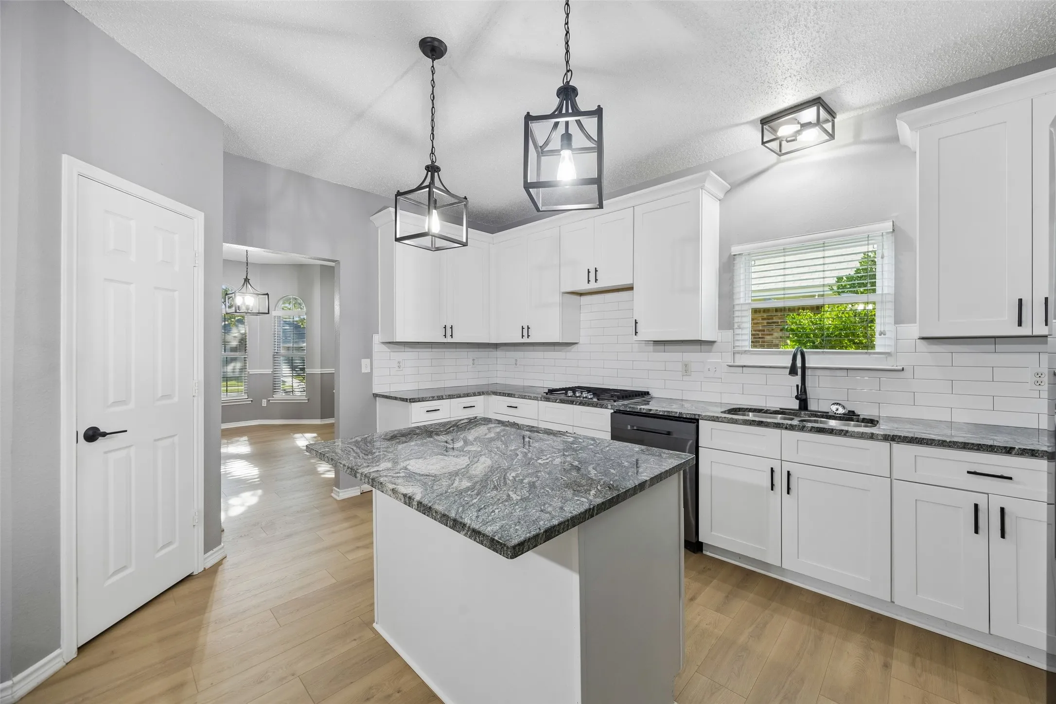 Kitchen featuring white shaker-style cabinetry, black hardware, subway tile backsplash, and a central island with a stone countertop
