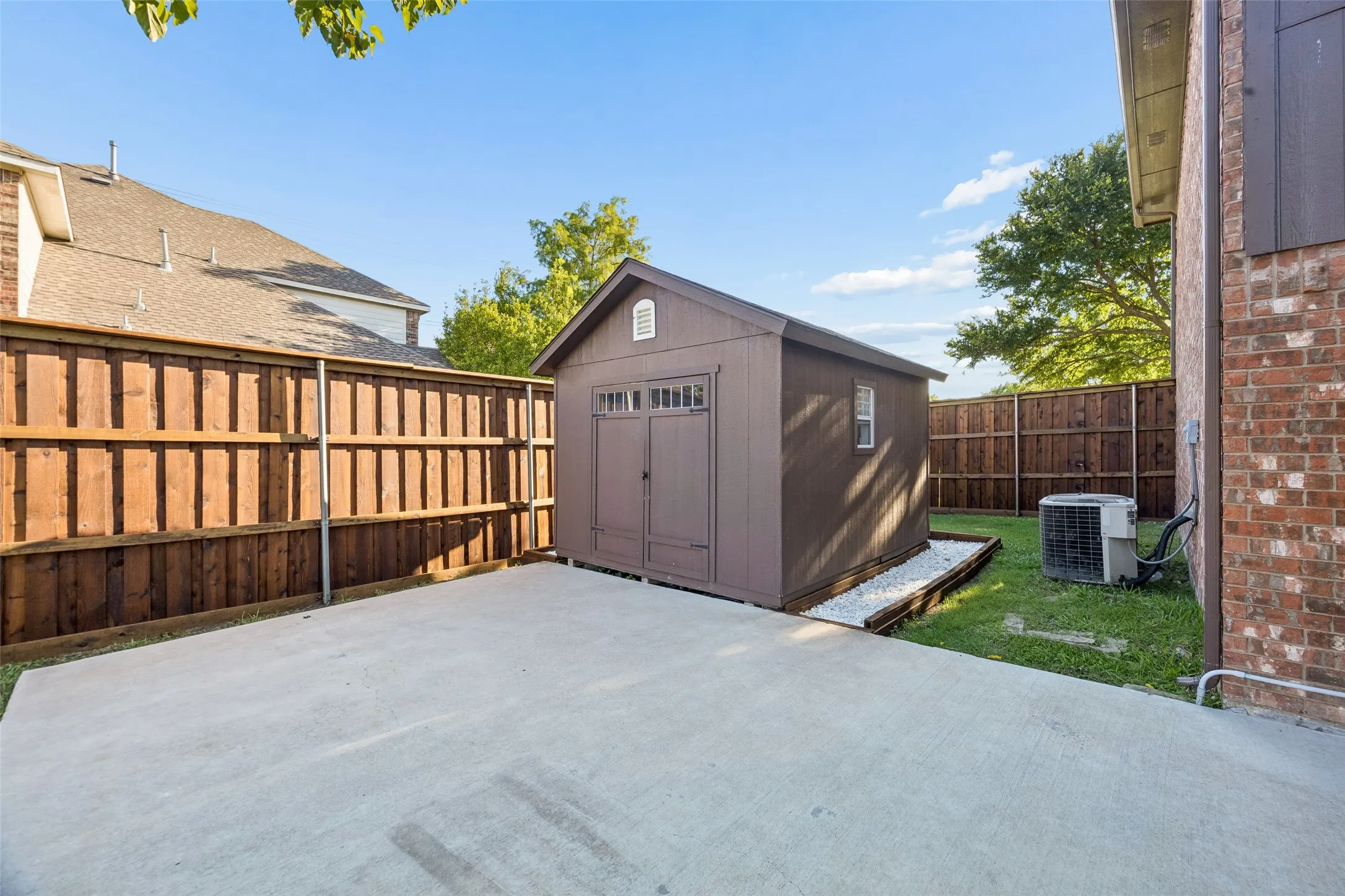 Concrete patio with a detached storage shed, wood privacy fencing, and a brick exterior wall
