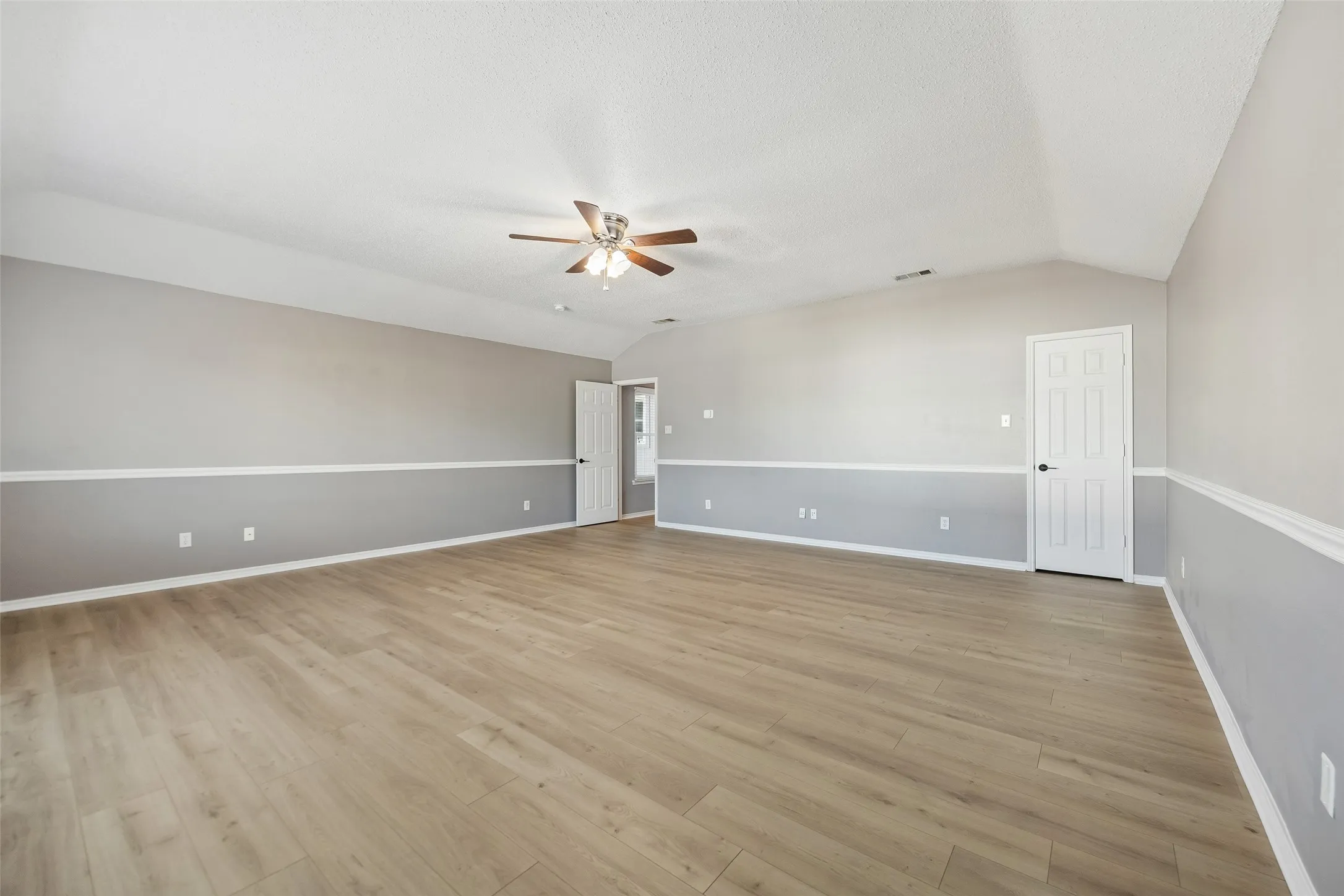 Vaulted ceiling, ceiling fan, wood-finish flooring, two-tone wall paint, interior doors