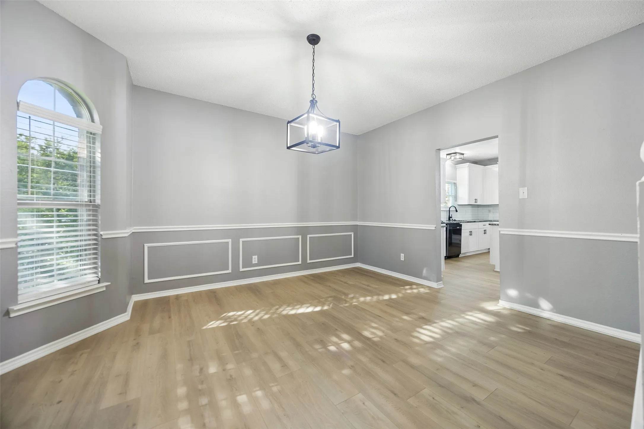 Wood-finish flooring, accent wall paneling, vaulted ceiling, arched window, and a contemporary light fixture