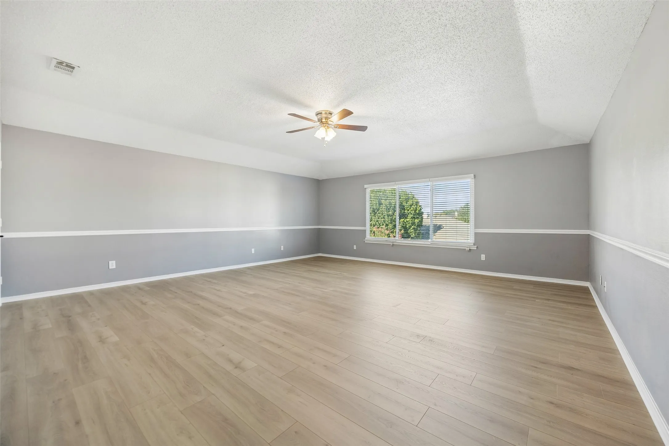 Spacious room featuring wood-finish flooring, a contemporary ceiling fan, and a large window
