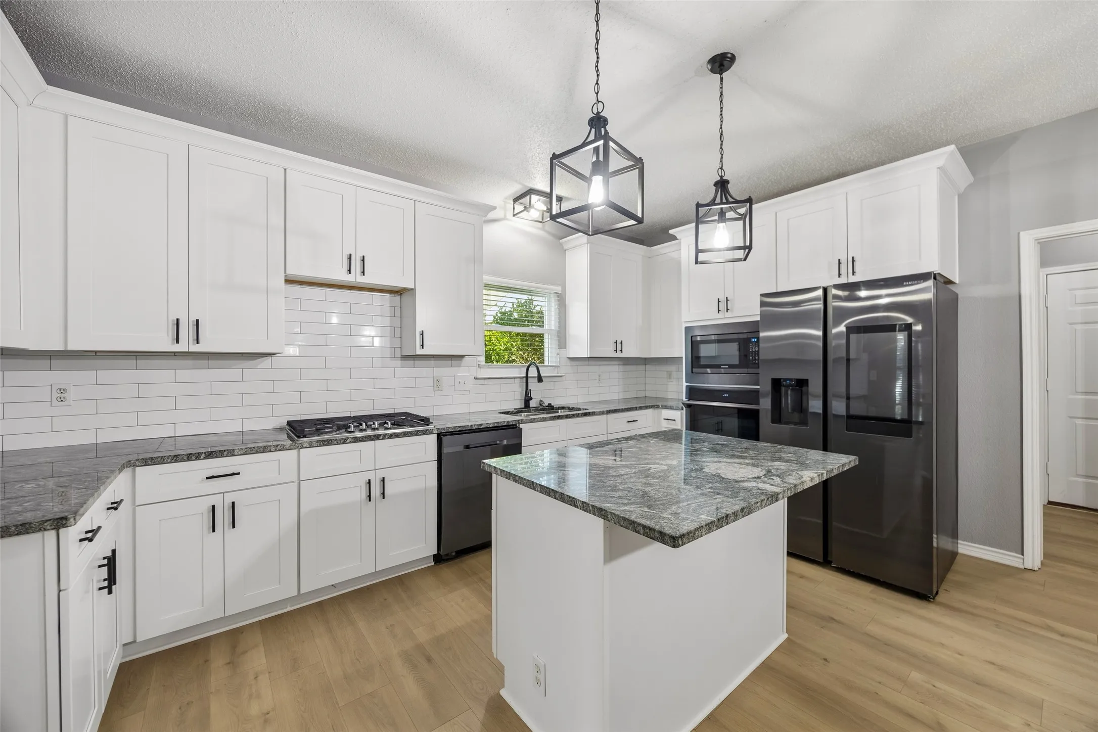 Kitchen featuring white shaker cabinets, subway tile backsplash, dark-toned appliances, and a central island with a stone-finish countertop