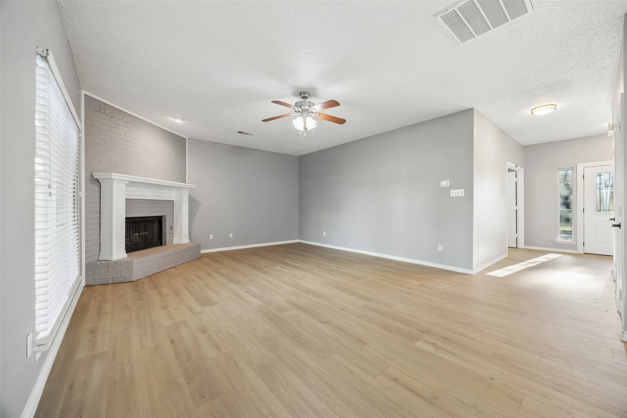 Spacious interior with wood-finish flooring, a painted brick fireplace with a white mantel, and a ceiling fan