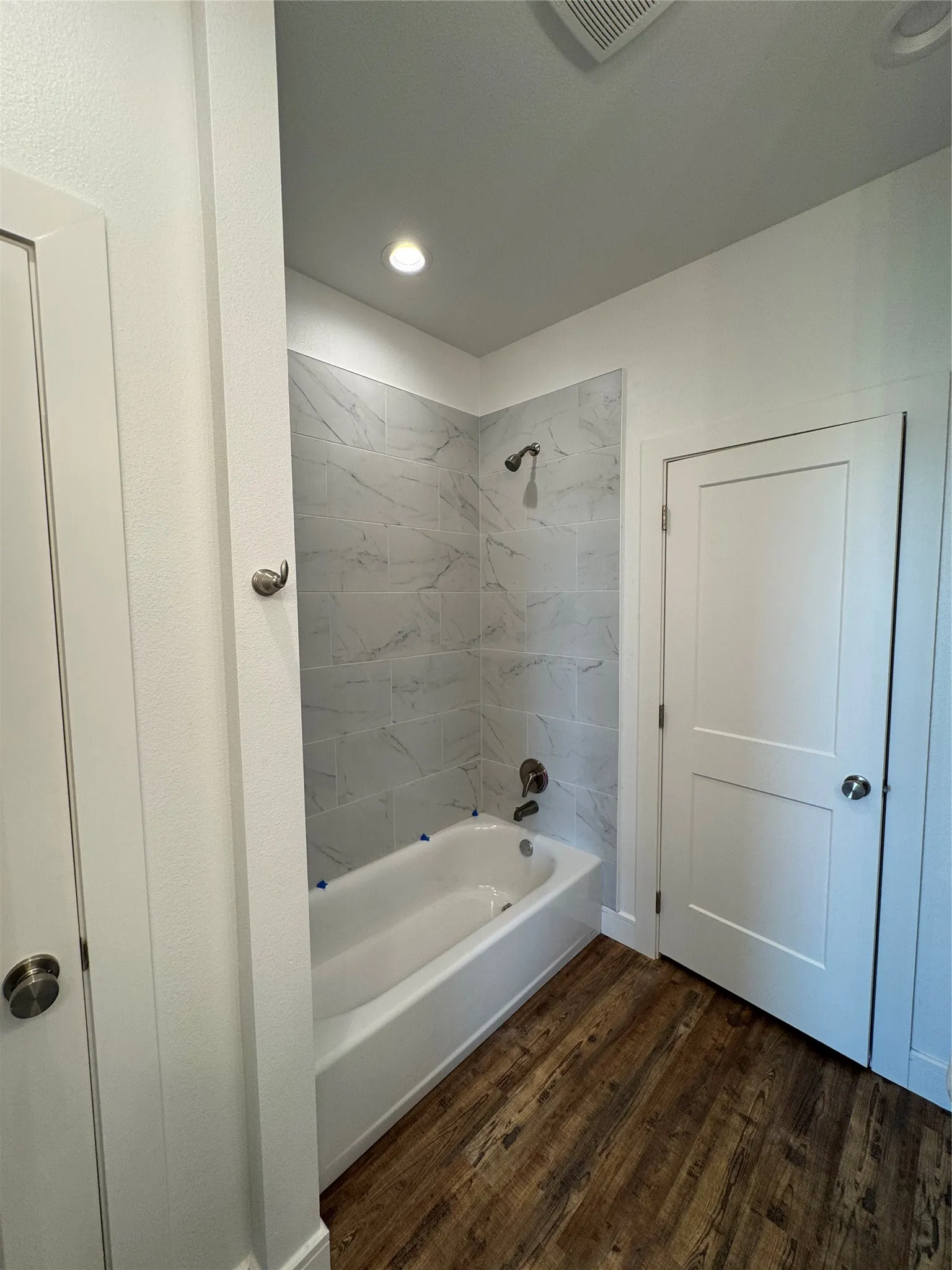 Bathtub with a shower fixture, white subway tile surround, wood-finish flooring, and recessed ceiling lighting