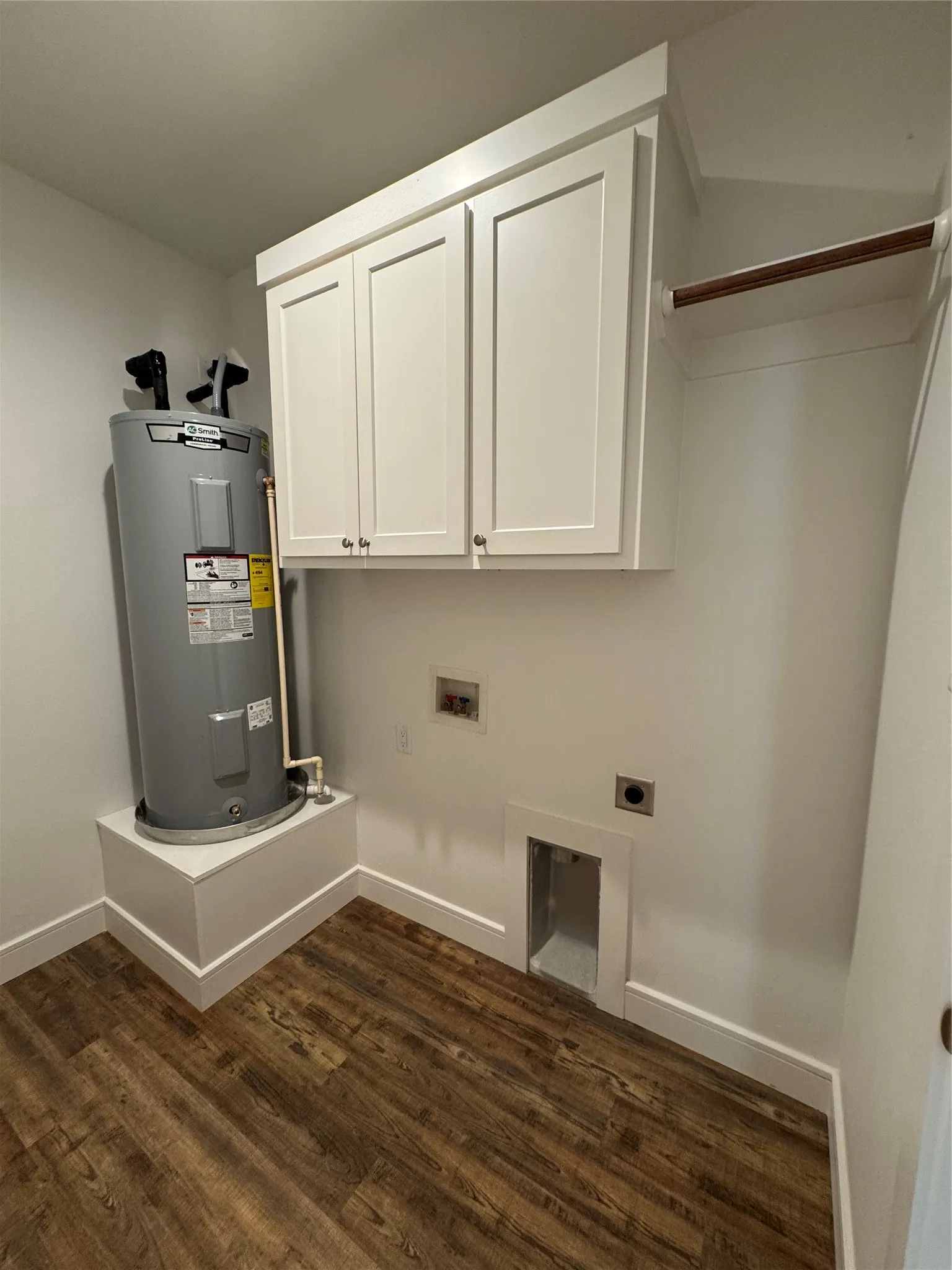 Wood-finish flooring, white cabinetry, built-in shelving, water heater, and utility hookups