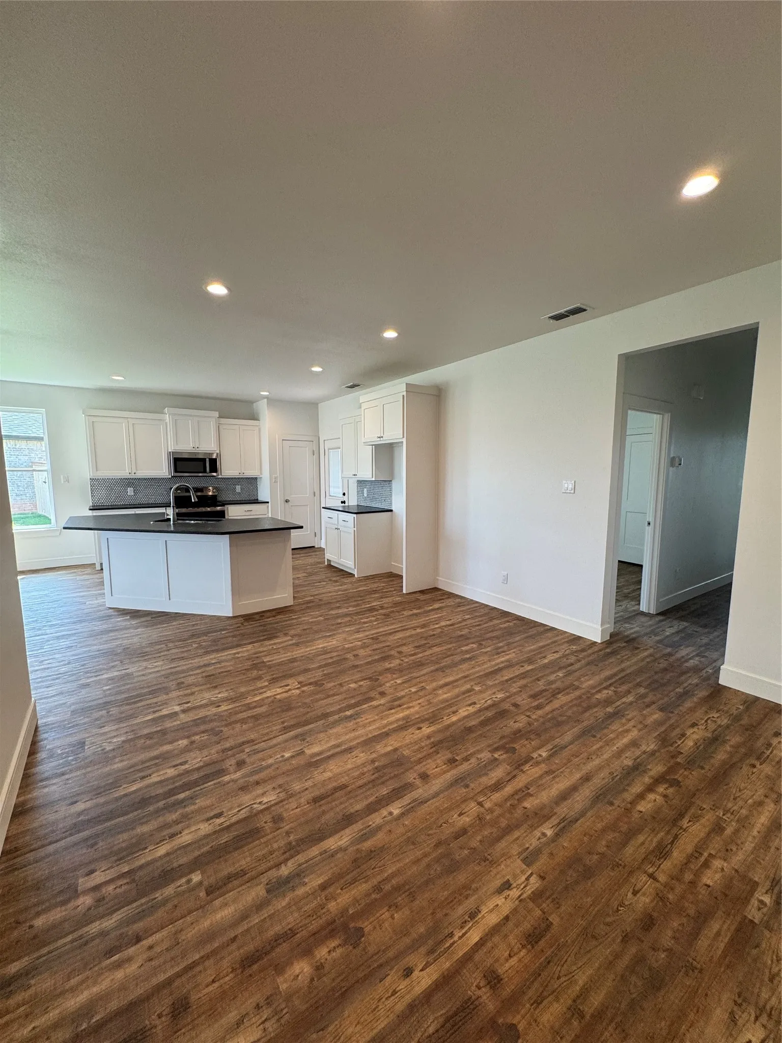 Open-concept living space featuring wood-finish flooring, recessed lighting, white cabinetry, a kitchen island with a dark countertop, and a dark tile backsplash