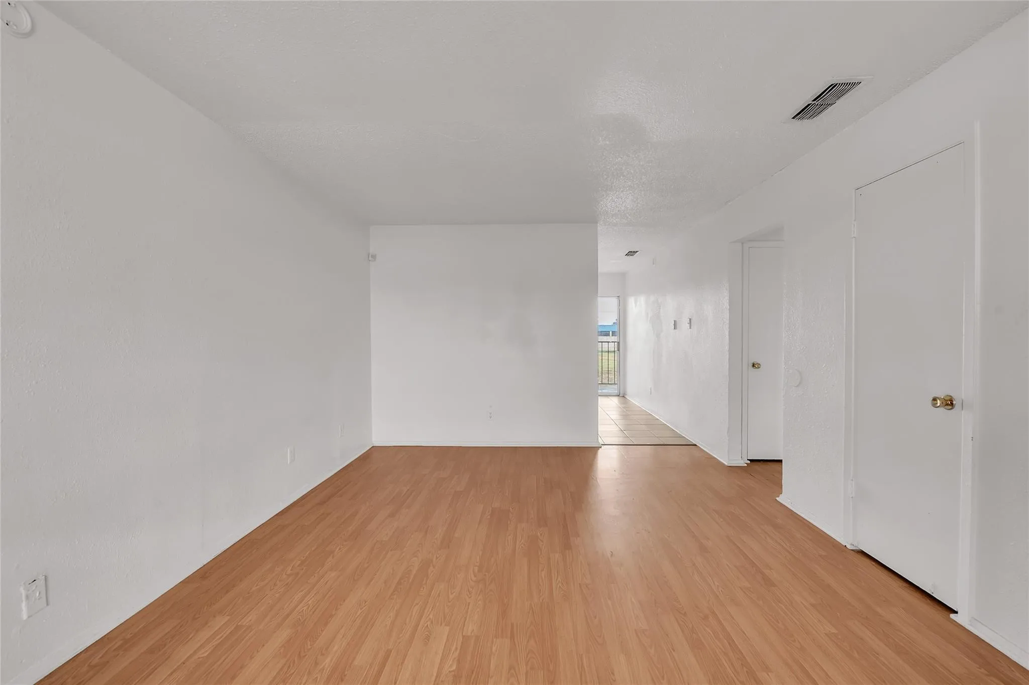 Wood-finish flooring throughout, bright white walls, and a recessed ceiling vent