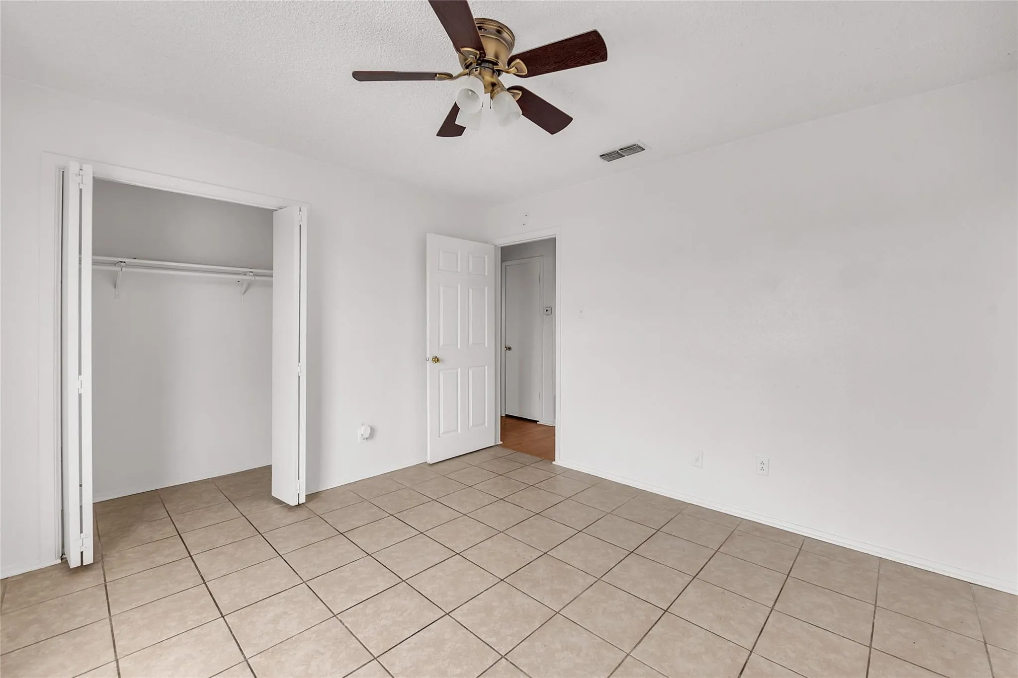 Tile flooring, ceiling fan with light fixture, white interior doors, and a built-in closet with bi-fold doors and shelving