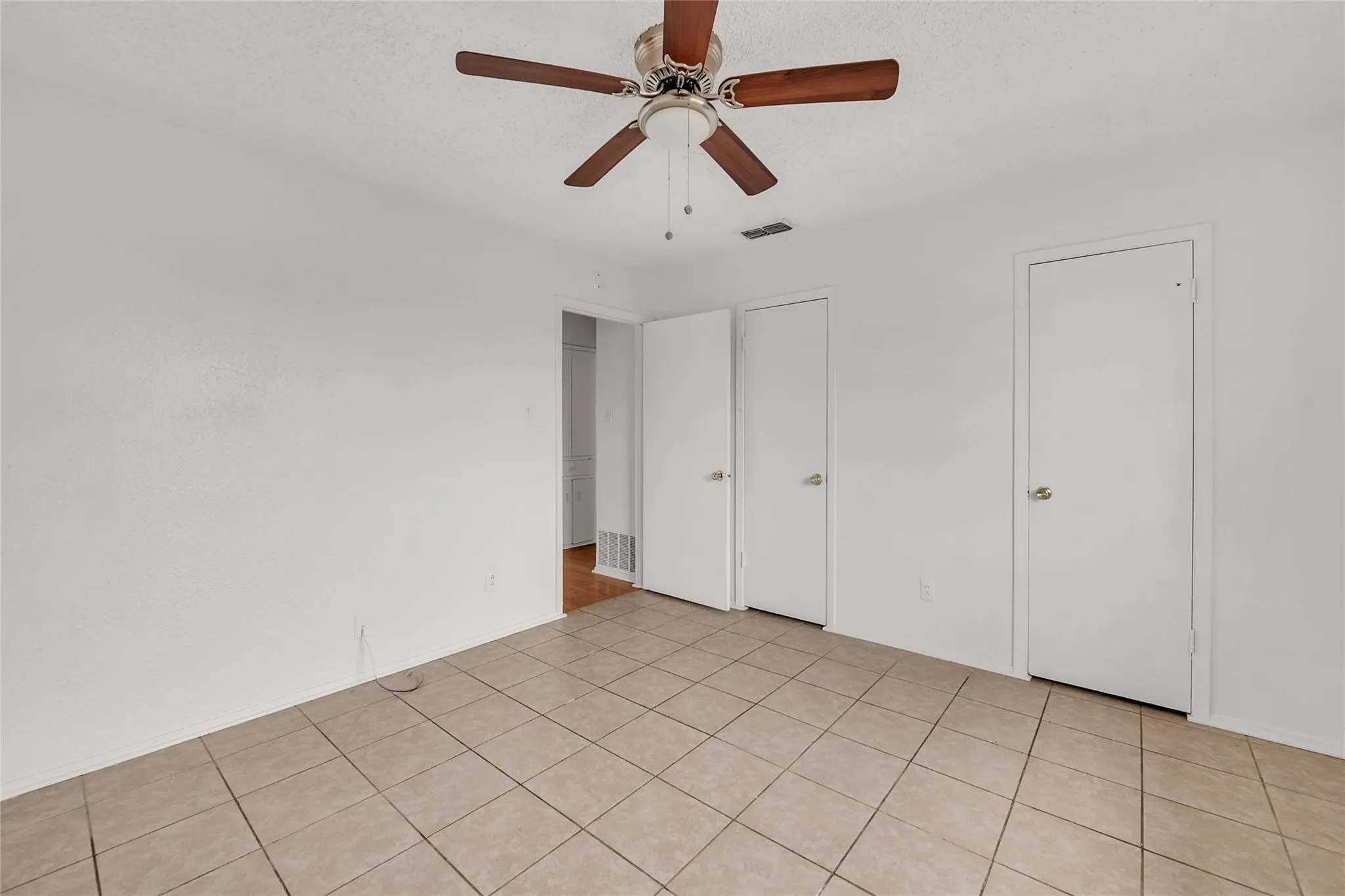 Neutral tone wall finishes, ceiling fan with wood-finish blades, and tile flooring