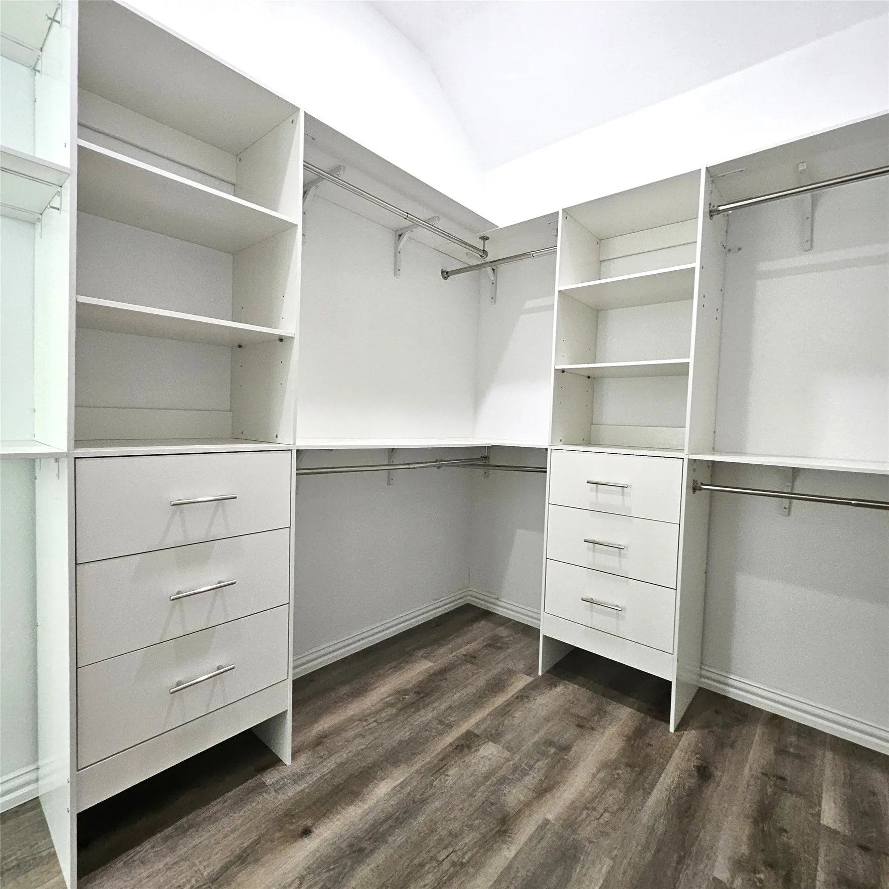 Custom white cabinetry with chrome hardware, integrated shelving, hanging rods, and wood-finish flooring