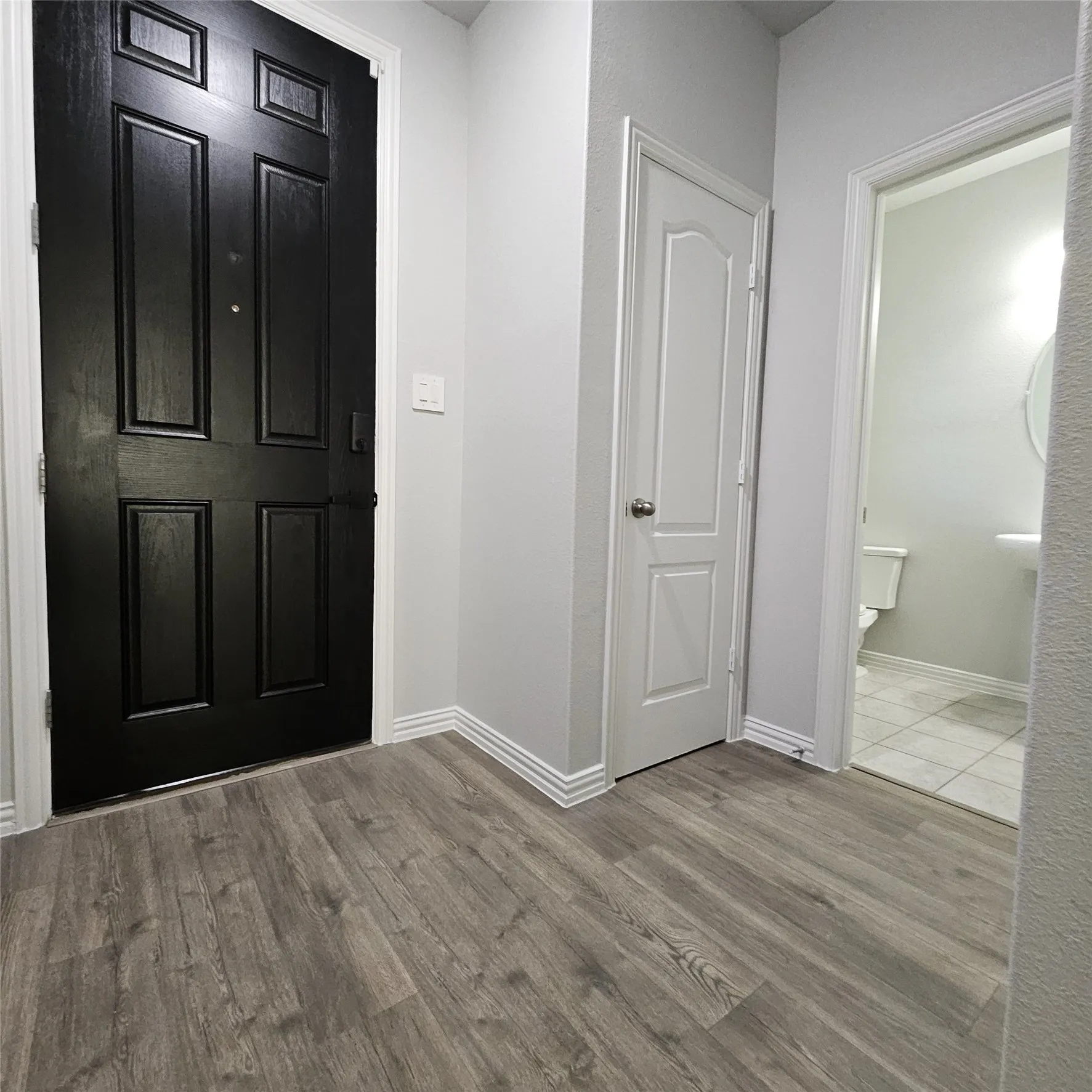 Panel-style entry door, wood-finish flooring, paneled interior door, white baseboards, and a pedestal sink in the powder room