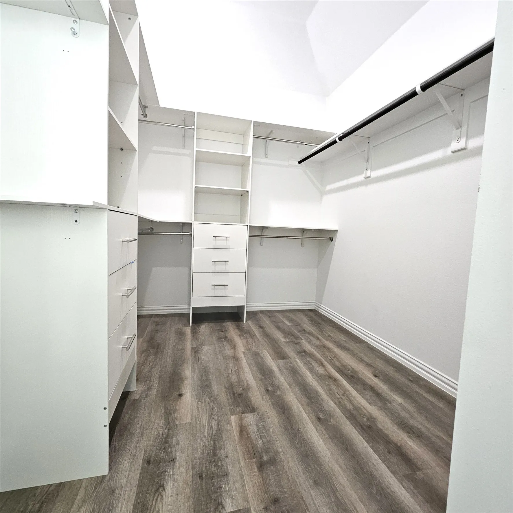 Walk-in closet featuring built-in shelving, integrated drawers, multiple hanging rods, and wood-finish flooring