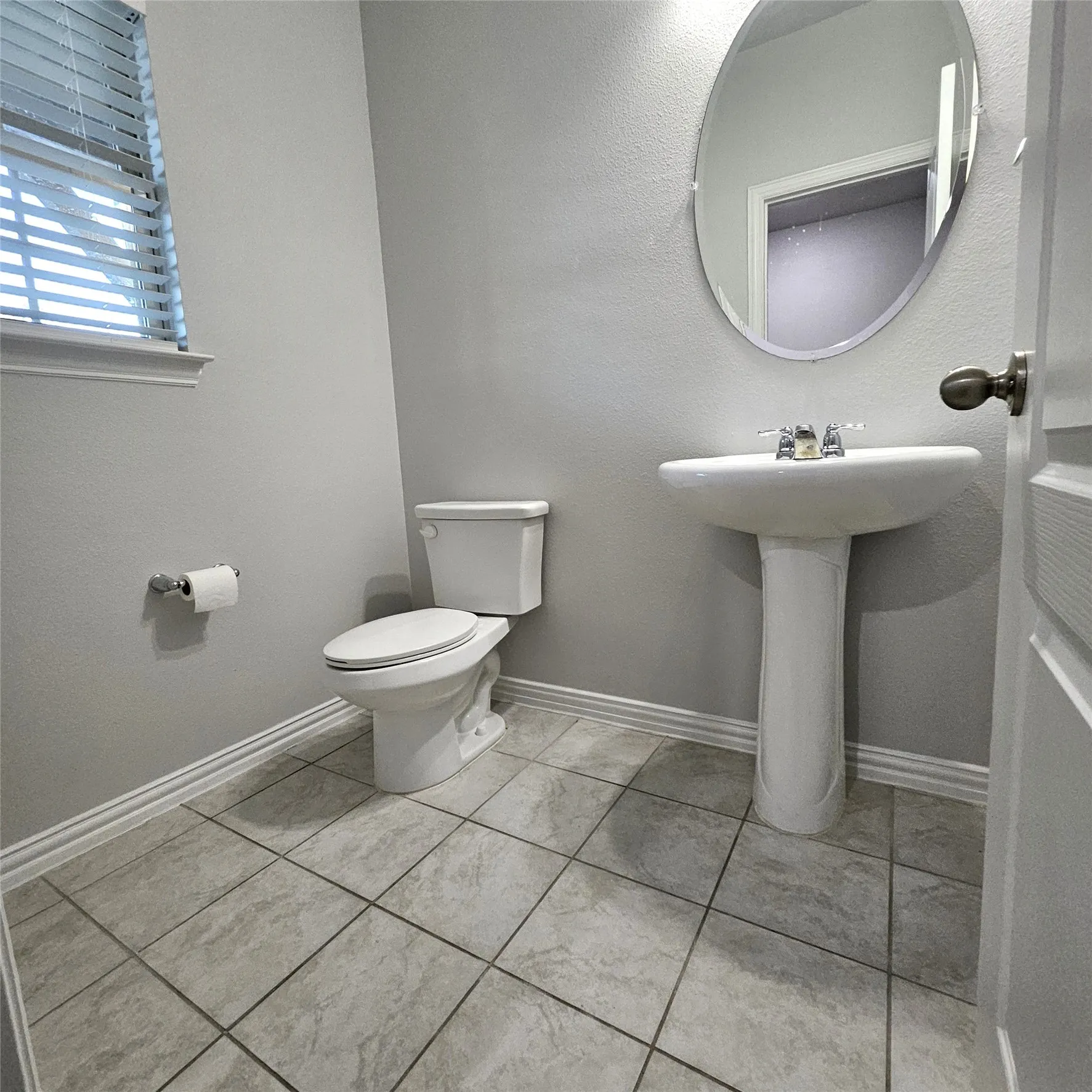 White pedestal sink with chrome faucet, white toilet, oval wall mirror, and tile flooring