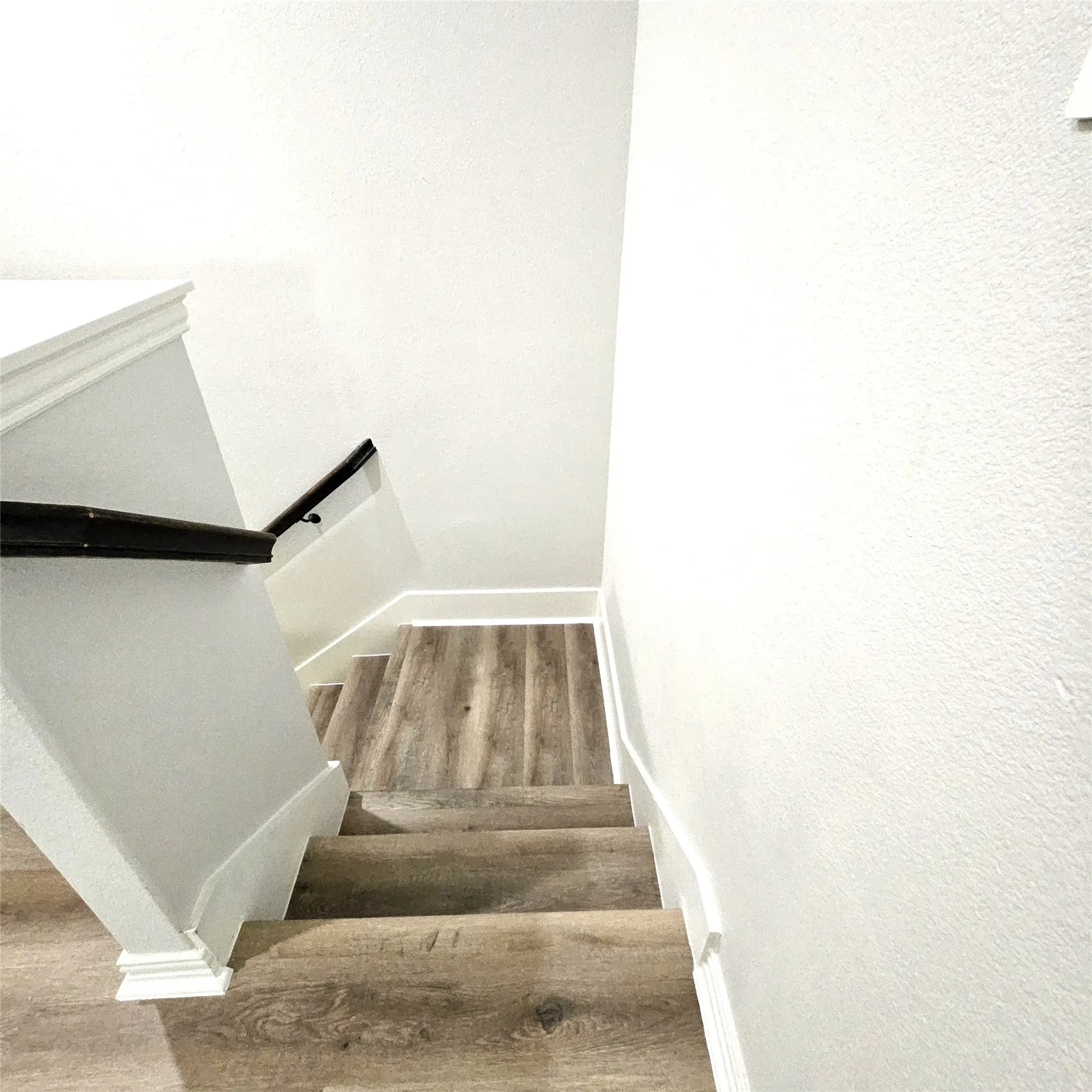 Staircase featuring wood-finish flooring, white risers, a dark wood-finish handrail, and white baseboards