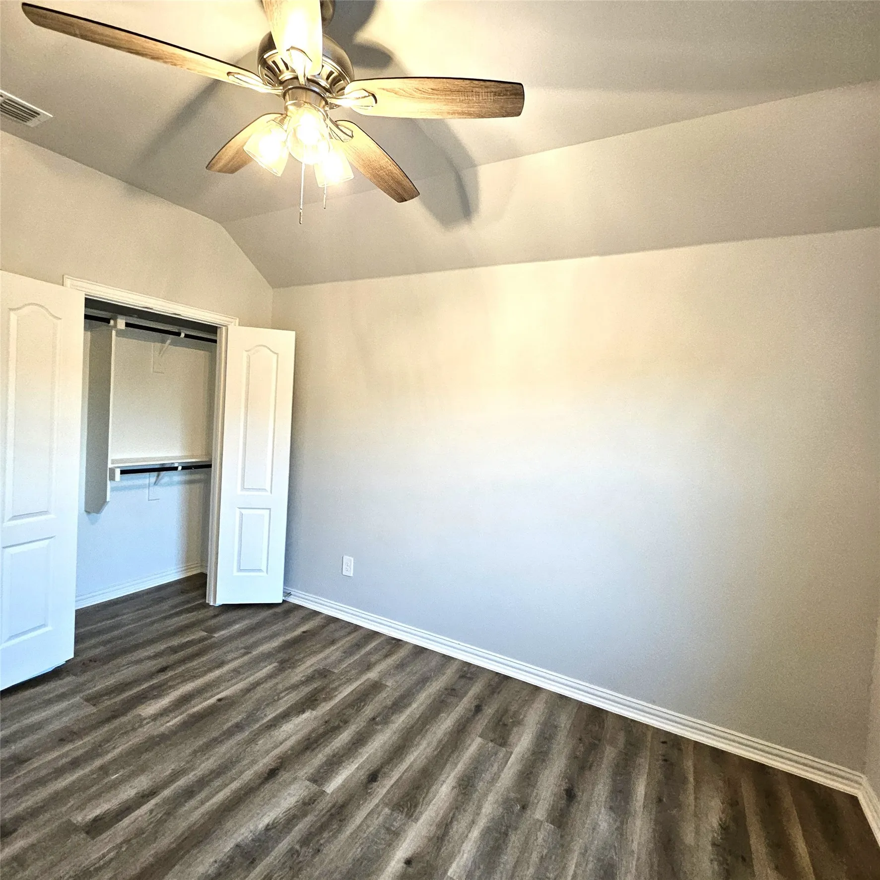 Vaulted ceiling featuring a ceiling fan with integrated lighting, wood-finish flooring, and a closet with bifold doors